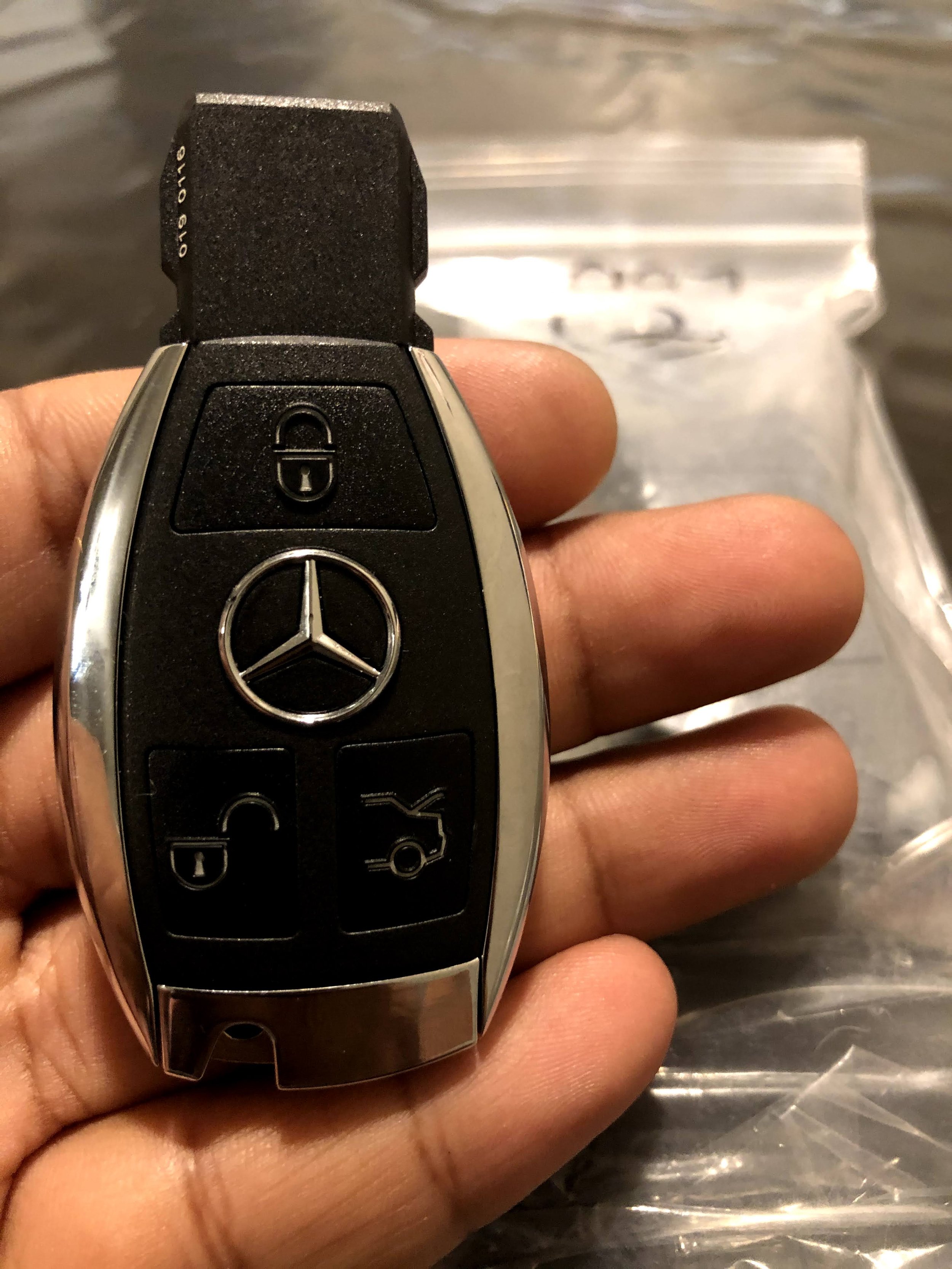 Close-up of a Mercedes-Benz car key being held between fingers, with a bag in the blurred background.