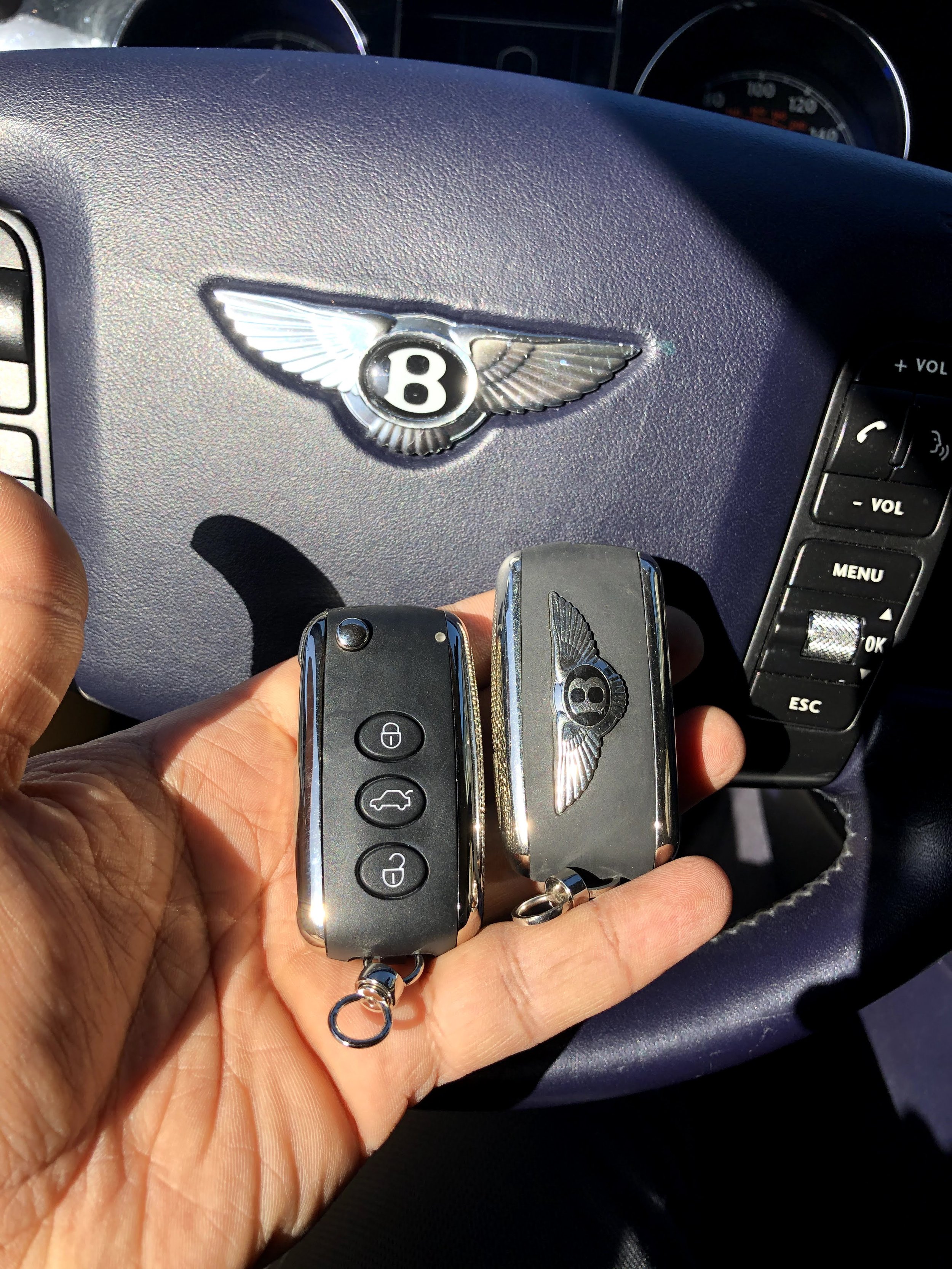 Person holding Bentley car keys in a car, with the Bentley logo visible on the steering wheel.