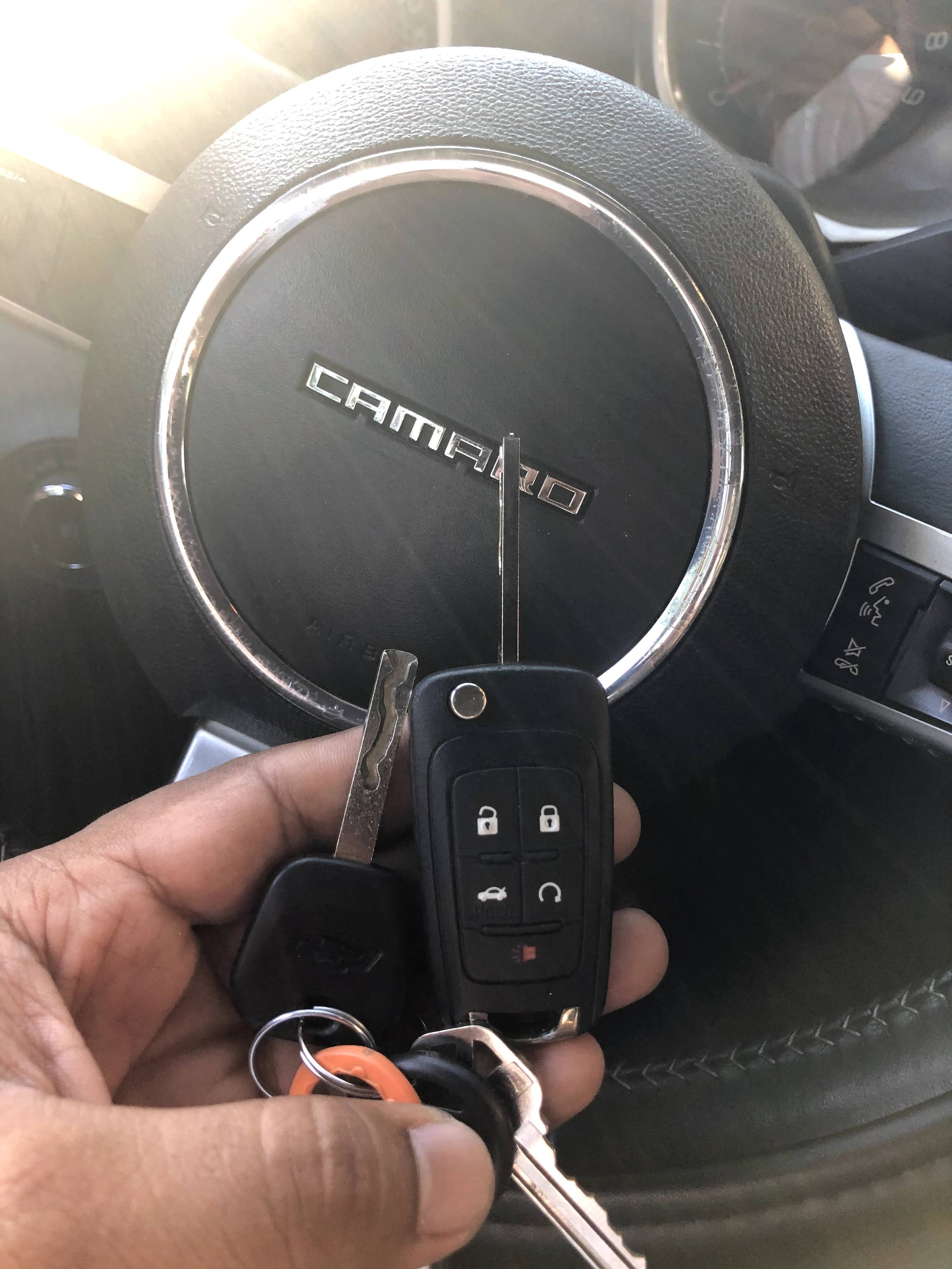 A person holding a car key in front of a black Toyota Camry steering wheel.
