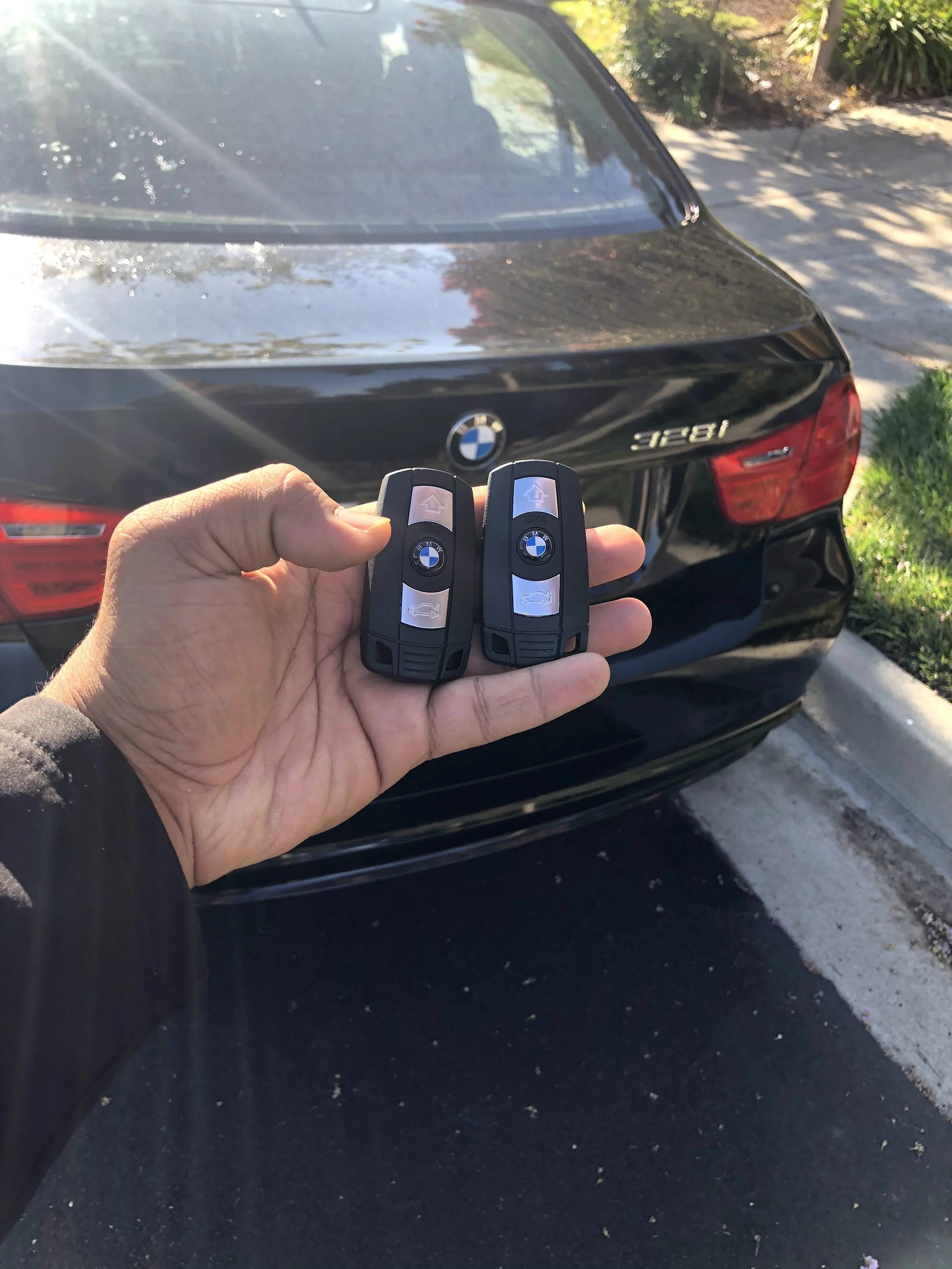 A person holding two BMW car keys in front of a black BMW car parked on the side of the road.