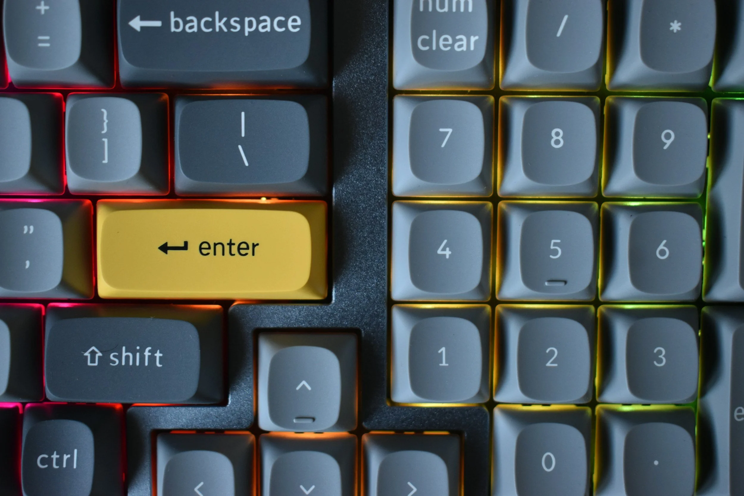 Close-up of a mechanical keyboard with multicolored backlighting, featuring a prominent yellow 'Enter' key in the center.