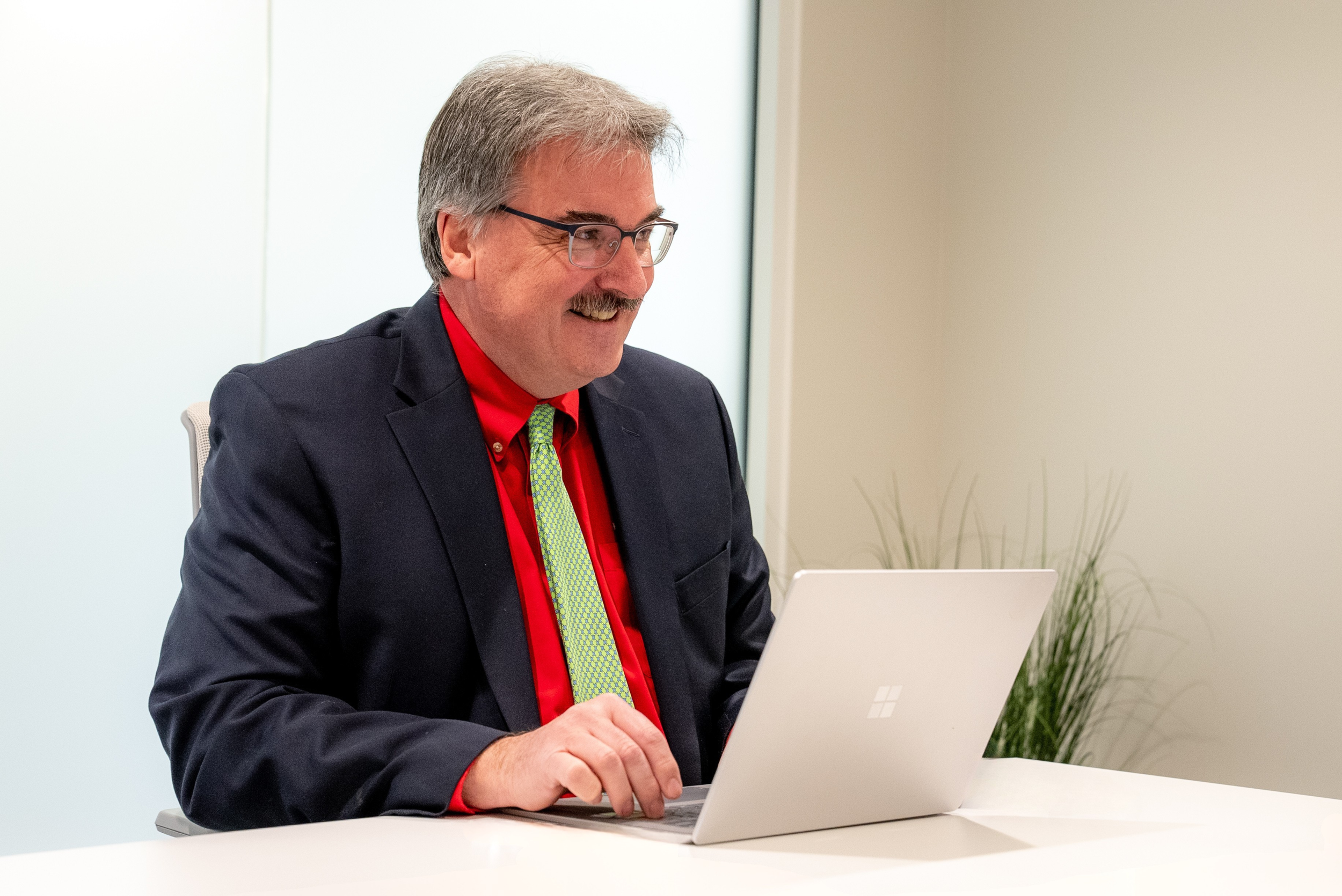 Smiling professional in a suit works on a laptop at a modern office desk.