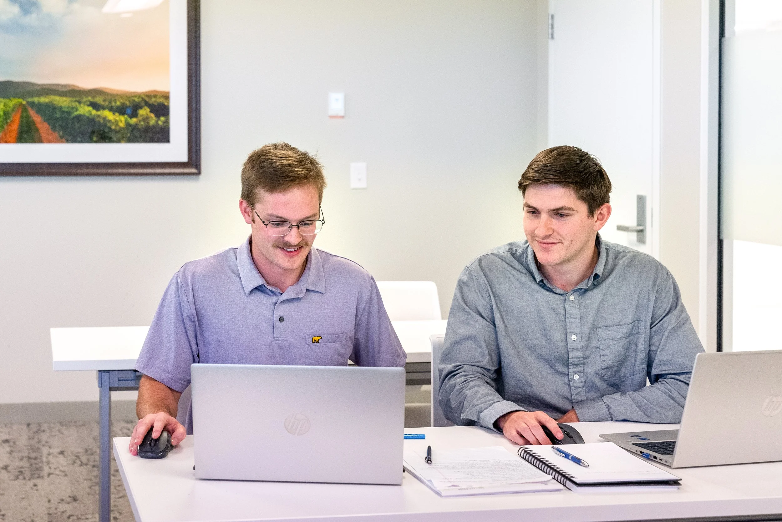 Two tax professionals working on laptops during a meeting in a CPA office, seated at a table with documents and natural lighting.