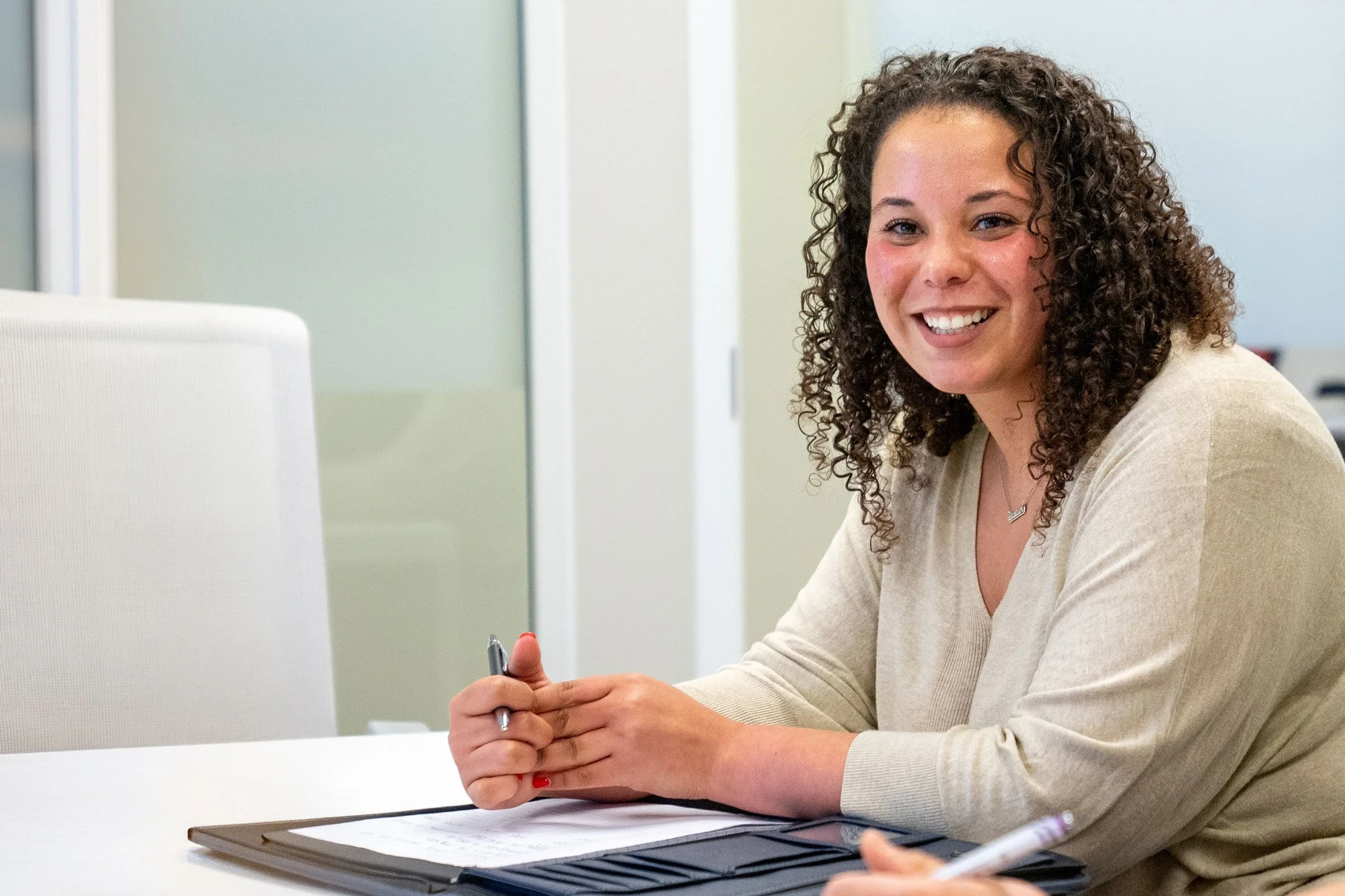 Tax professional smiling while seated at a conference table, holding a pen during a client meeting.