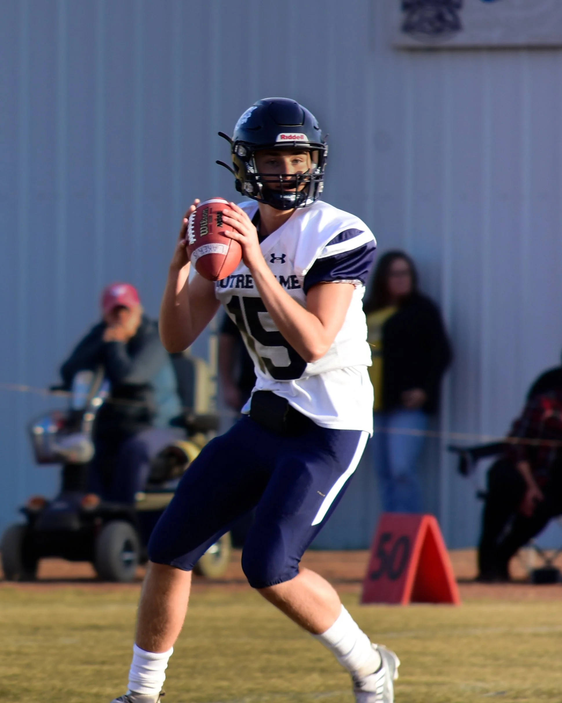 Young football player wearing a black helmet and white jersey holding a football on a field.