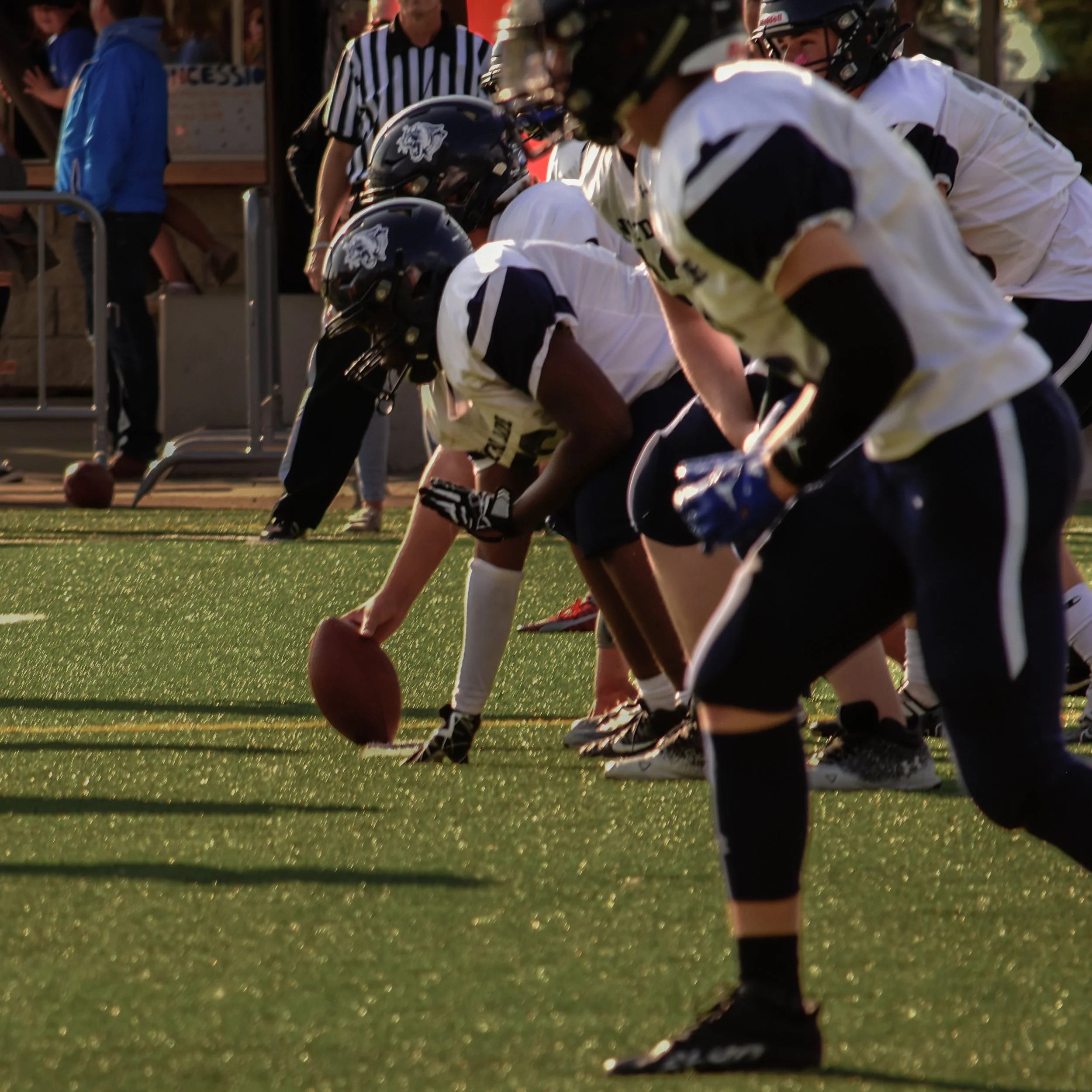 Football players lined up at the line of scrimmage during a game on a sunlit field.