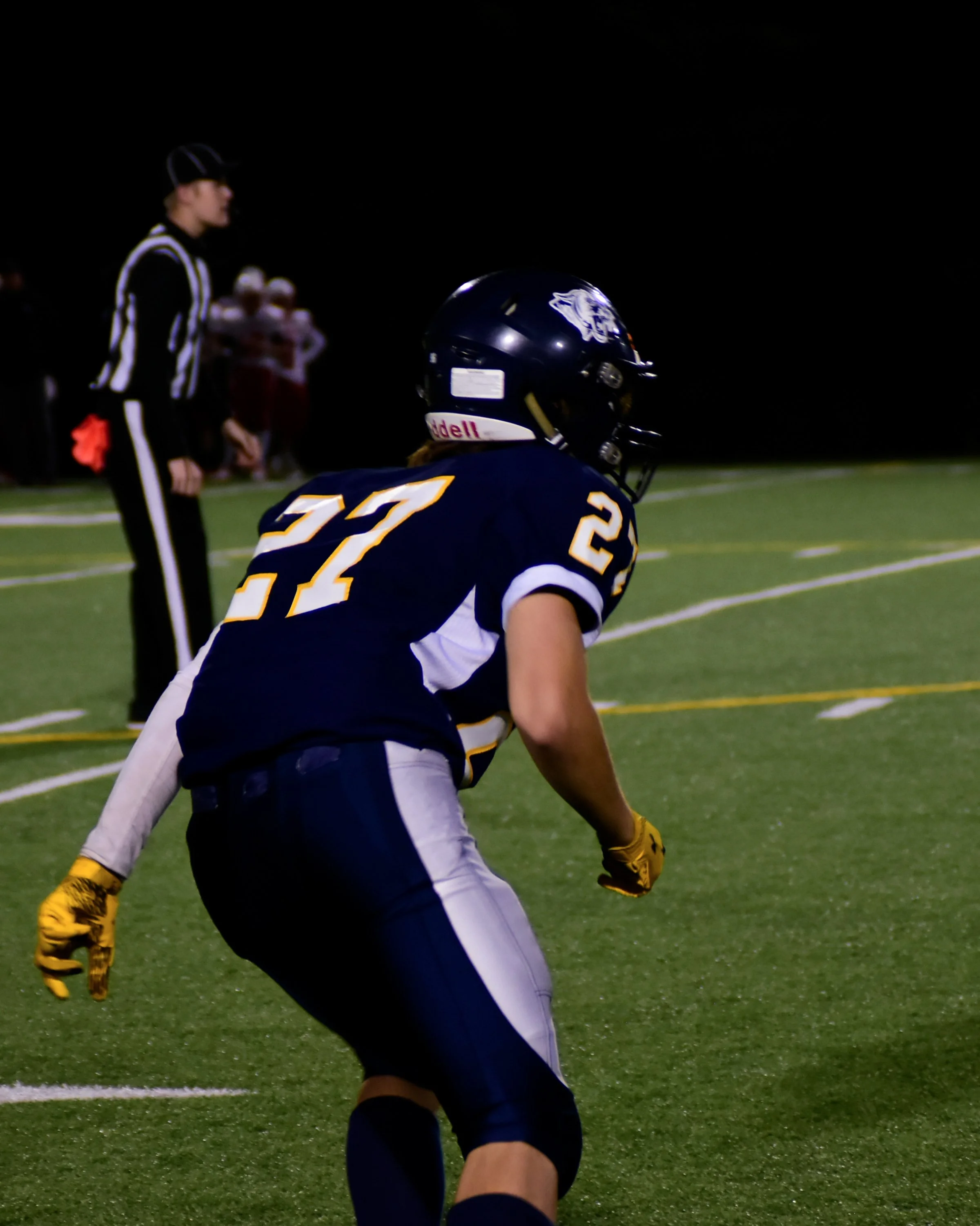 Football player wearing jersey number 22 preparing to move on the field during a night game, with a referee and other players in the background.