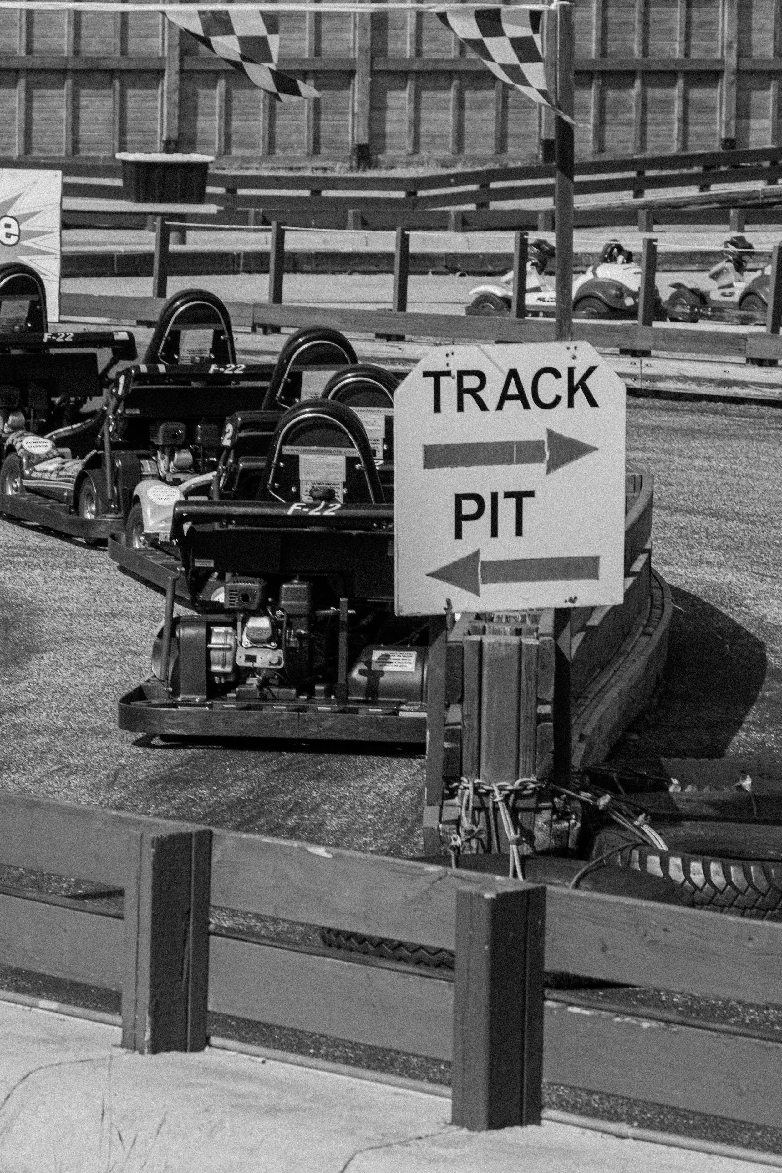 Go-karts parked at a racing track with a sign indicating directions to the track and pit area.