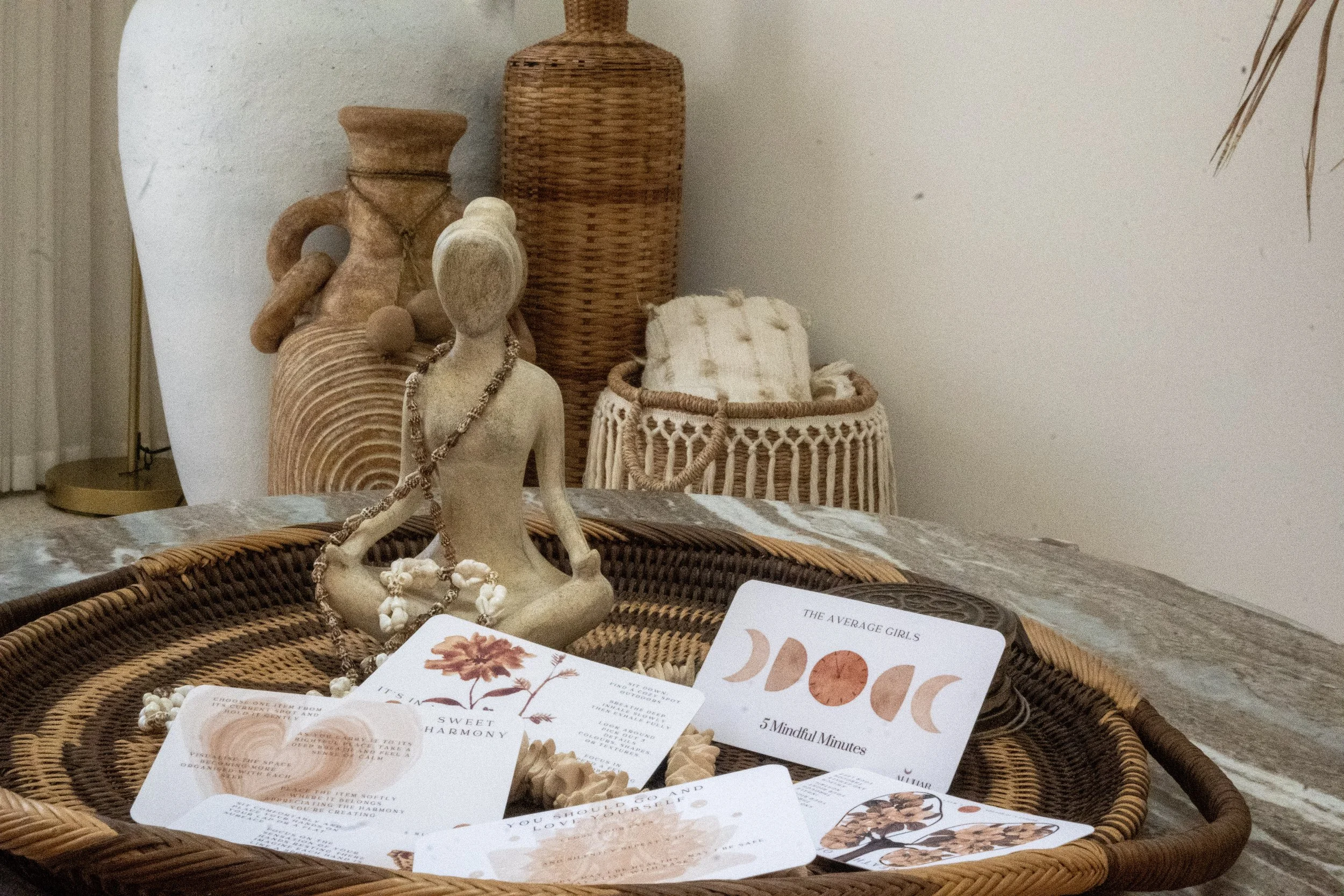 Boho decor scene with a wicker basket containing a figurine, seashells, and cards; background features woven and ceramic vases.