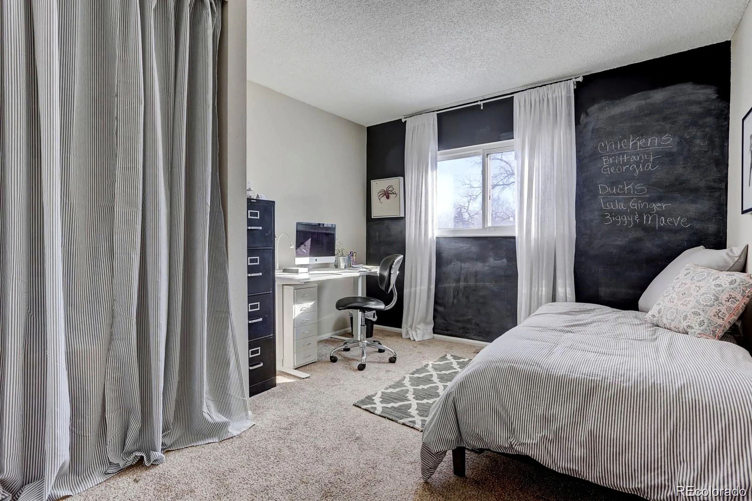 A small office room with day bed. Lightweight ceiling-to-floor draperies replace plastic accordion doors that hide a utility eyesore and some extra storage, softening the otherwise wasted area and tying in the bed linens. A full wall of chalkboard