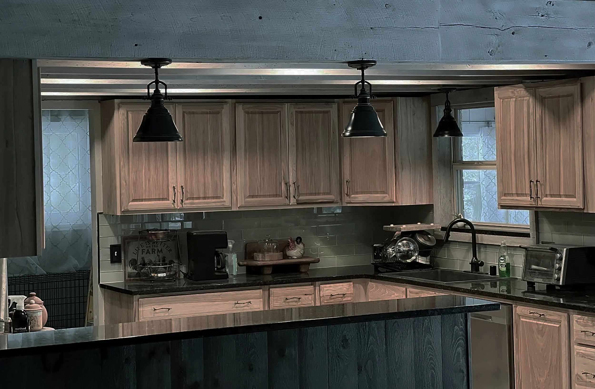 Adding a reclaimed header piece at the transition into the kitchen resolves an awkward situation since the ceiling was removed. Nesting pancake lights on the rustic ceiling pieces, between the joists, lifts the eye beyond the joists into the void, a