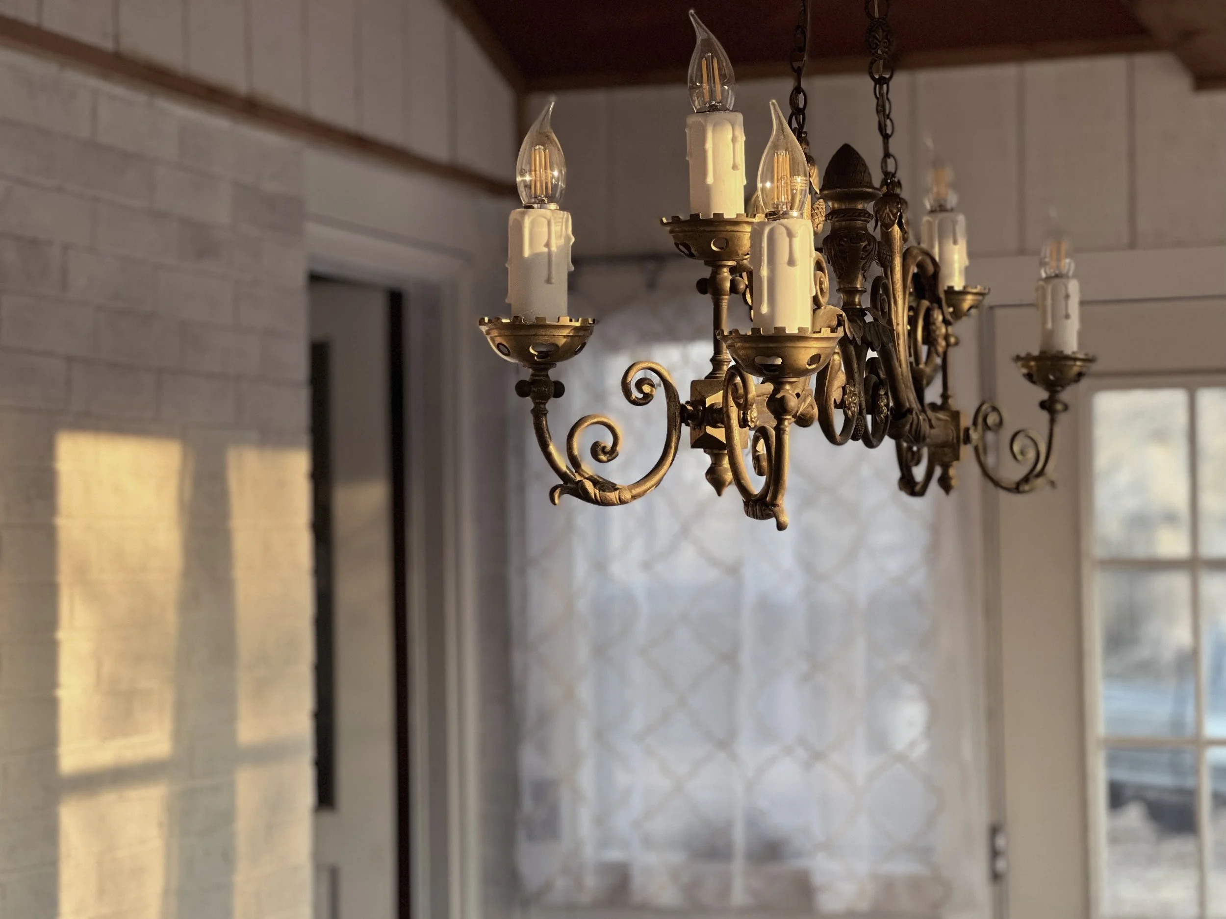 Whitewashed brick and shiplap, although not at all original in farmhouse style, is dressed up here, transitioning a casual sun room into a dedicated dining or party room. Complimentary flat-gold patterned sheer curtains add an upscale-yet-airy privac