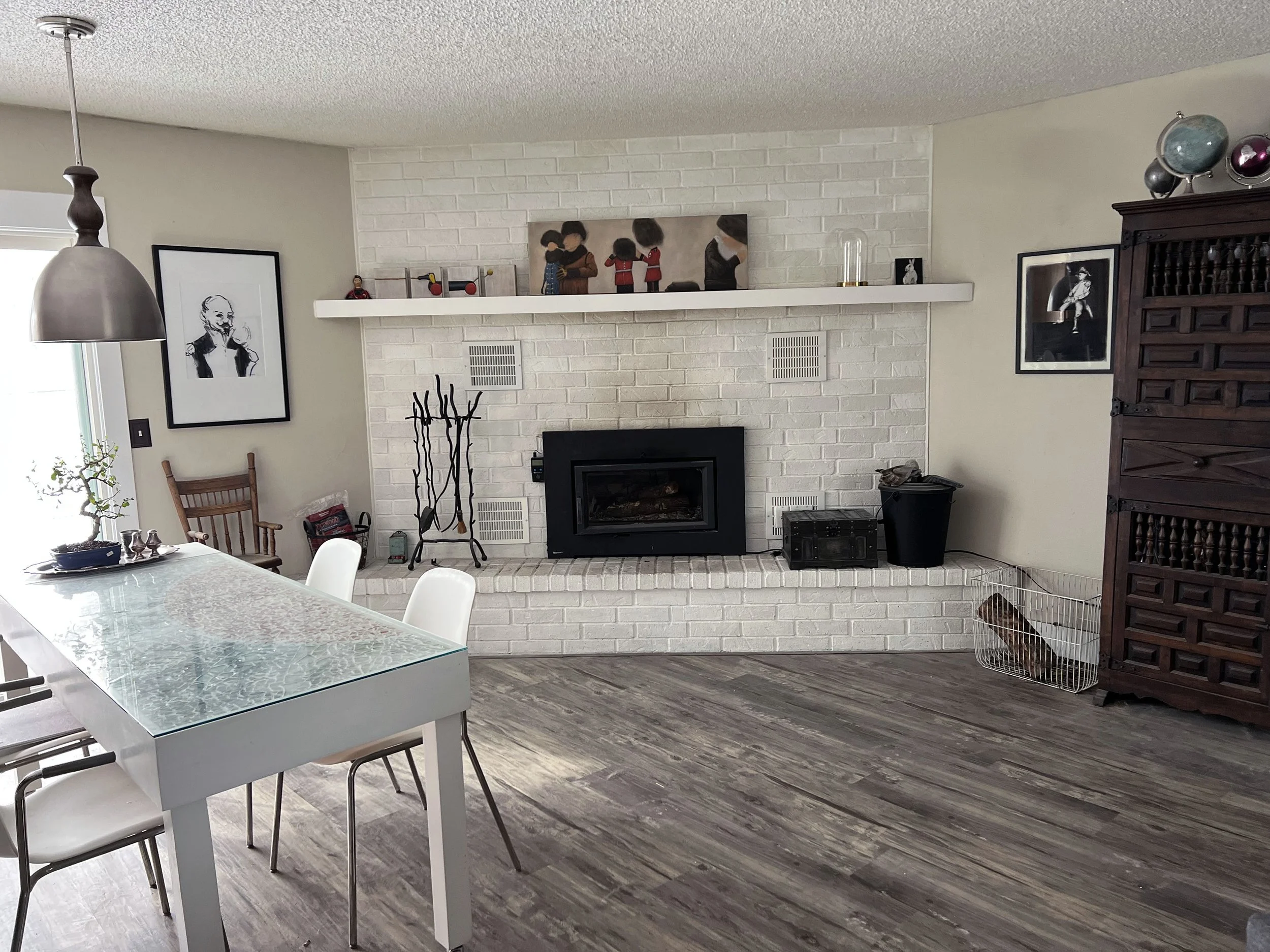 The brick is painted out with a light hand and slightly thinned-out paint to keep some brick texture in tact. Awkward stove insert is replaced by a contemporary flat model with glass for fire viewing. Flooring and wall colors are reconciled through