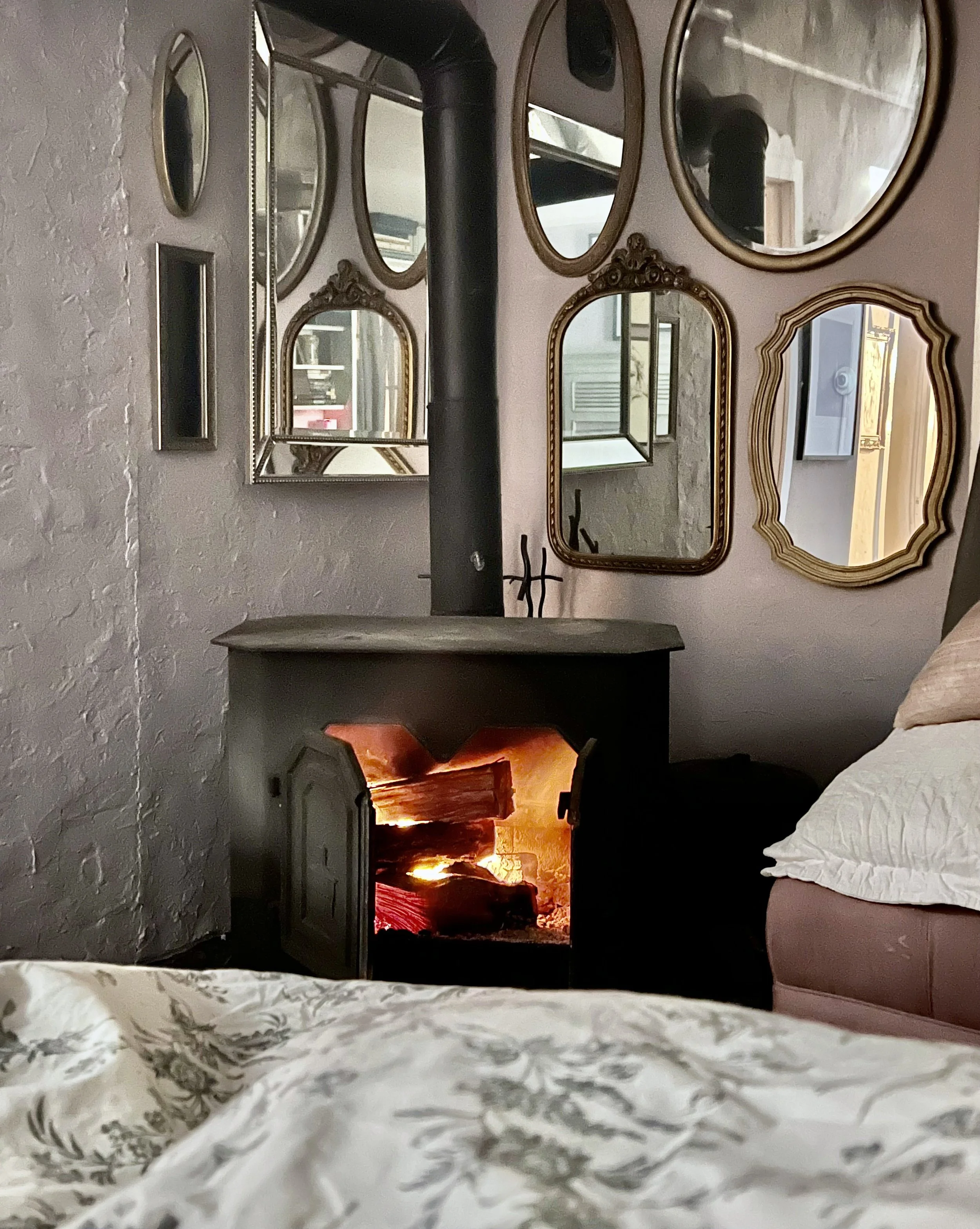 A collection of antique gold-framed mirrors surrounding the fireplace riser integrates the stove area with the rest of a very whimsical bedroom. Additionally, mirrors are great for bouncing light around a darker room.