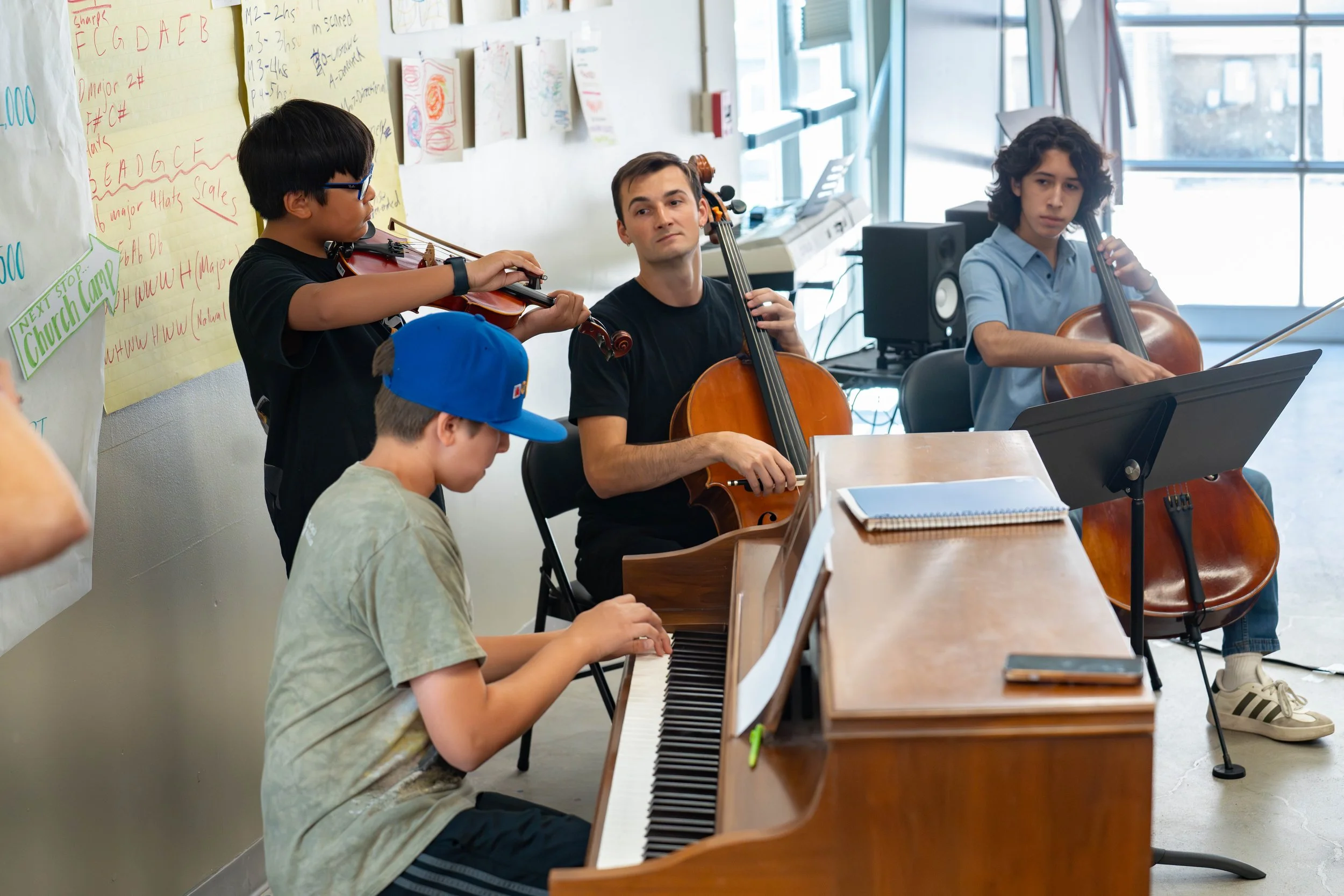 Peter playing the cello with a small group of students at the Santa Clarita valley youth orchestra performer composer workshop. Musicians are playing Cello, Violin, and Piano
