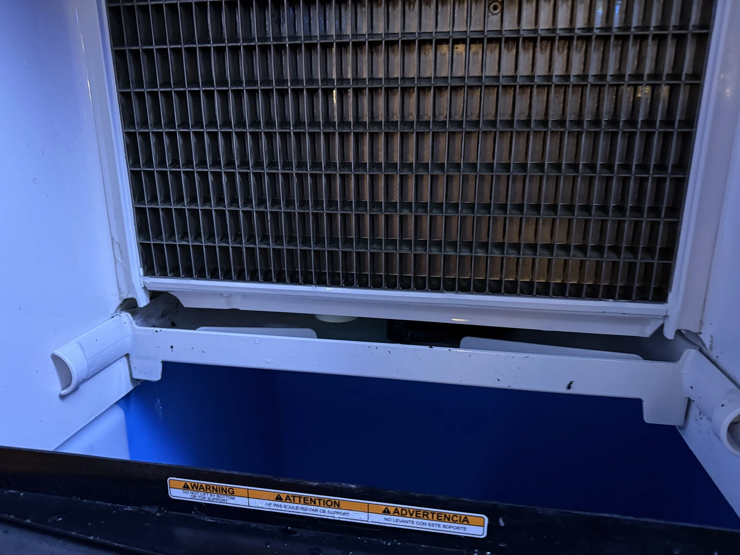 Close-up of a white vending machine with metal coin slides and a warning label, featuring compartments behind a metal grate.