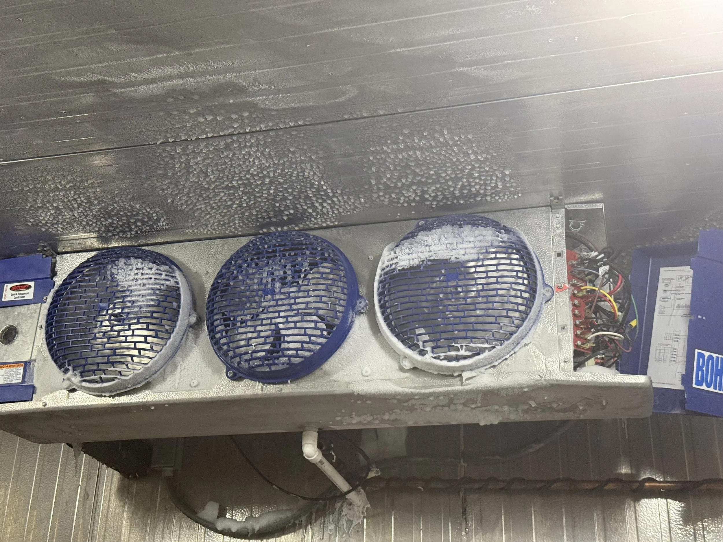 View of a metallic surface with water droplets and condensation, with three blue rollers or fans at the bottom and some electrical wiring visible on the right side.