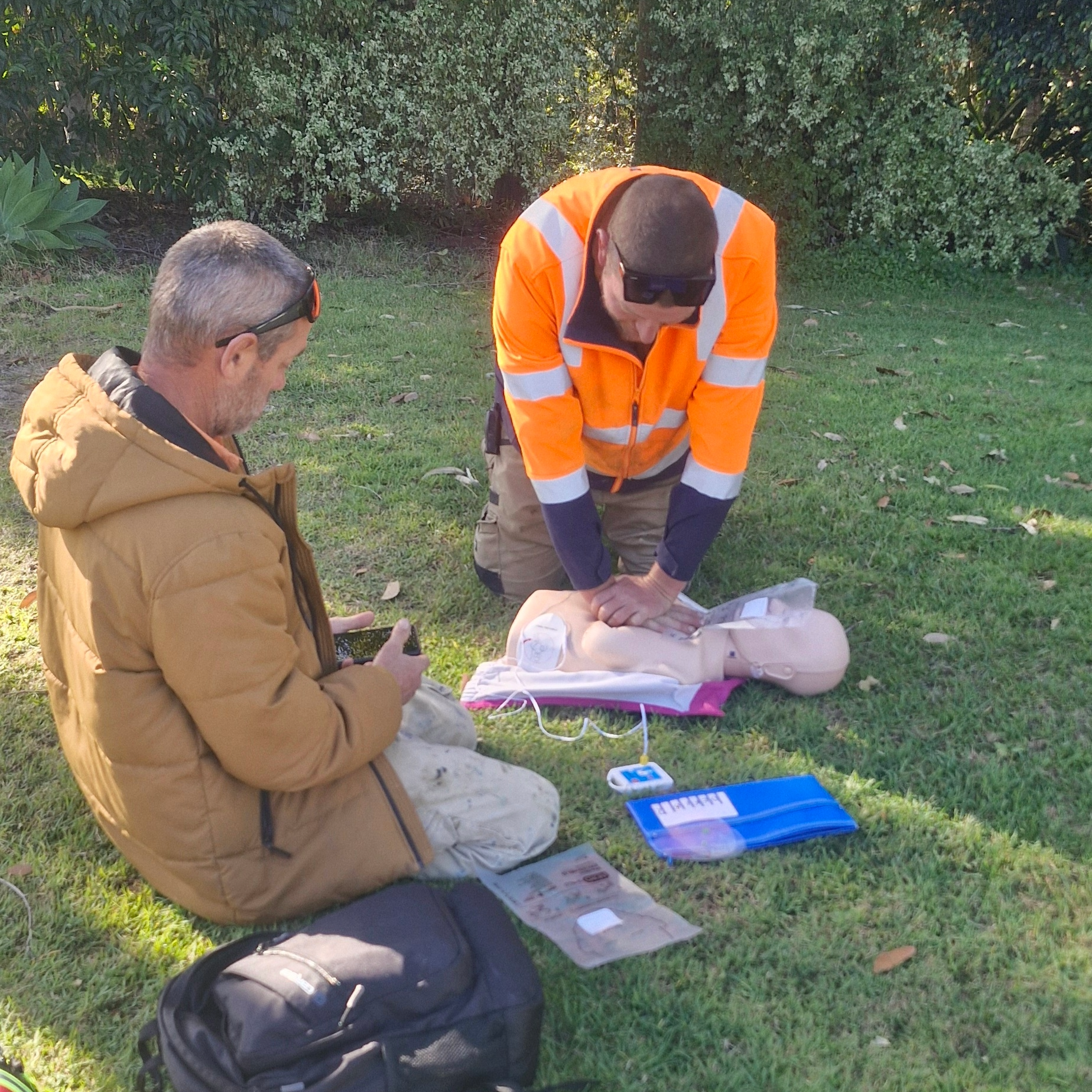 Person practicing CPR on a training mannequin with a focus on chest compressions on a wooden floor.
