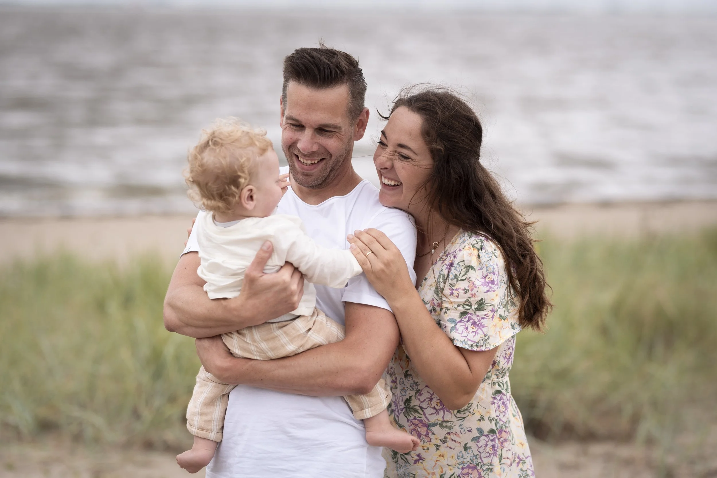 Ein glückliches Paar mit einem kleinen Kind am Strand, lachend und sich umarmend.