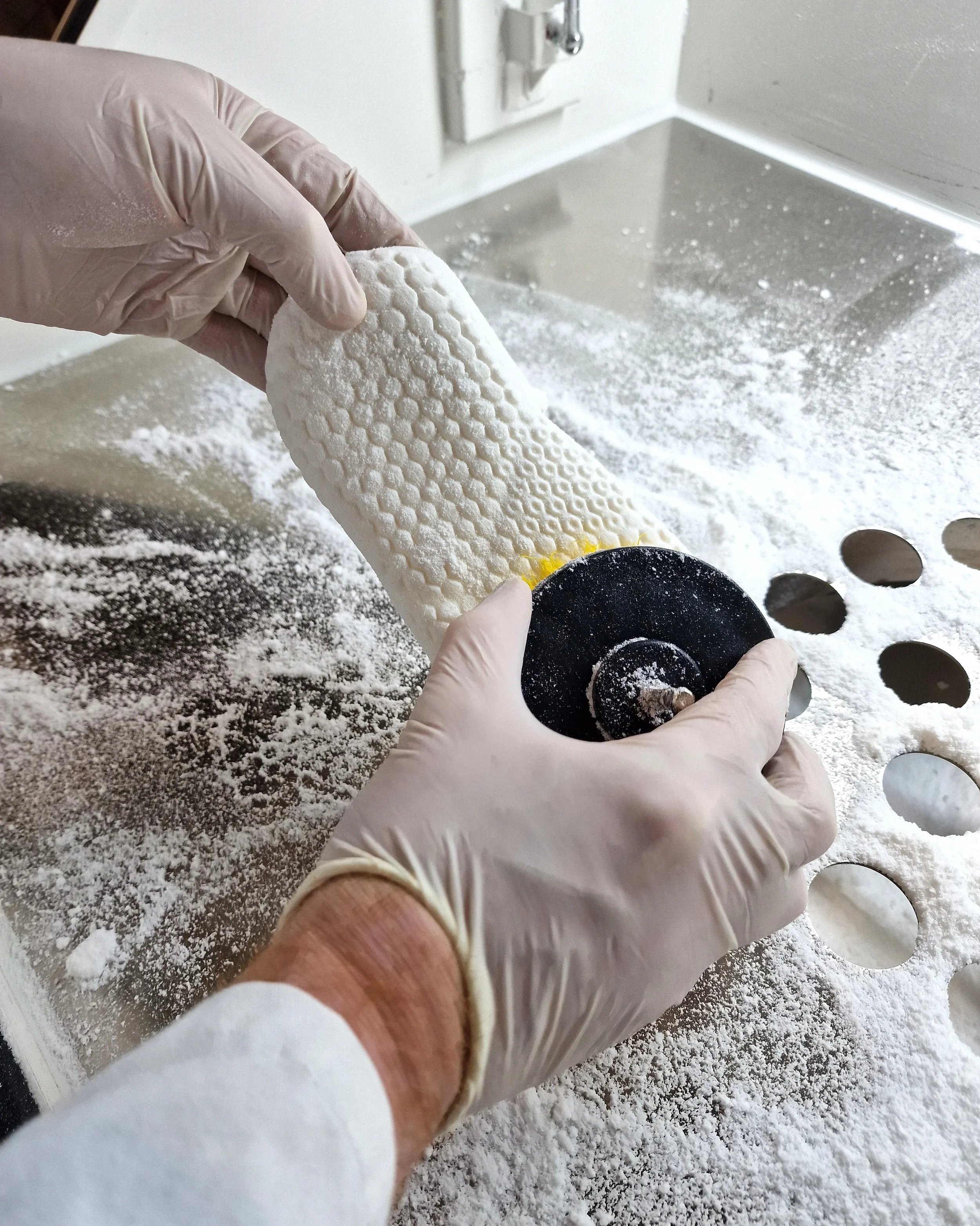 Close-up of gloved hands manually post-processing a white 3D-printed shoe sole, illustrating the labor-intensive finishing required in hybrid footwear manufacturing.