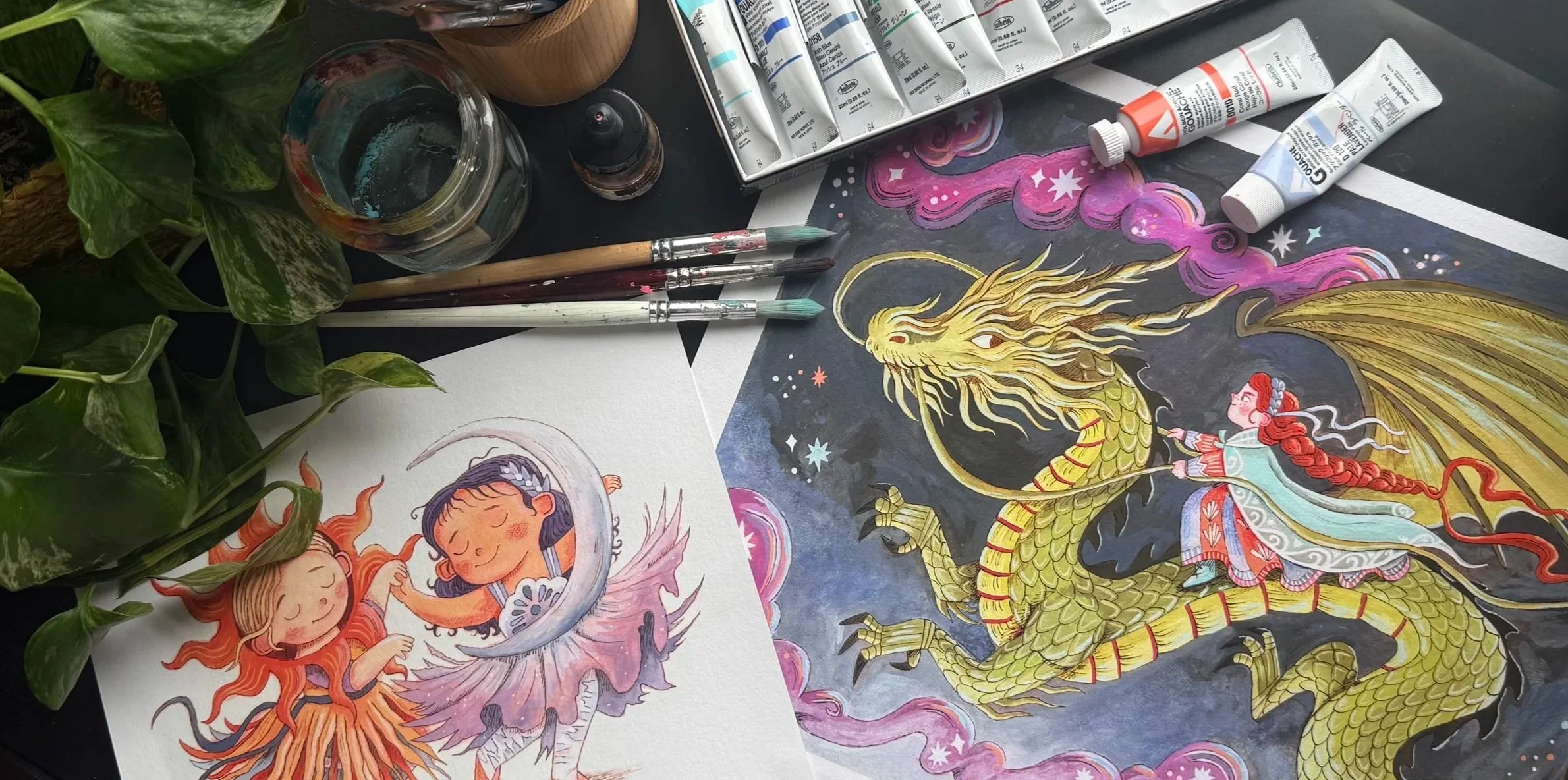 Art supplies on a table including brushes, paints, and illustrated artwork featuring a girl with red hair riding a golden dragon, surrounded by pink and purple clouds and stars.