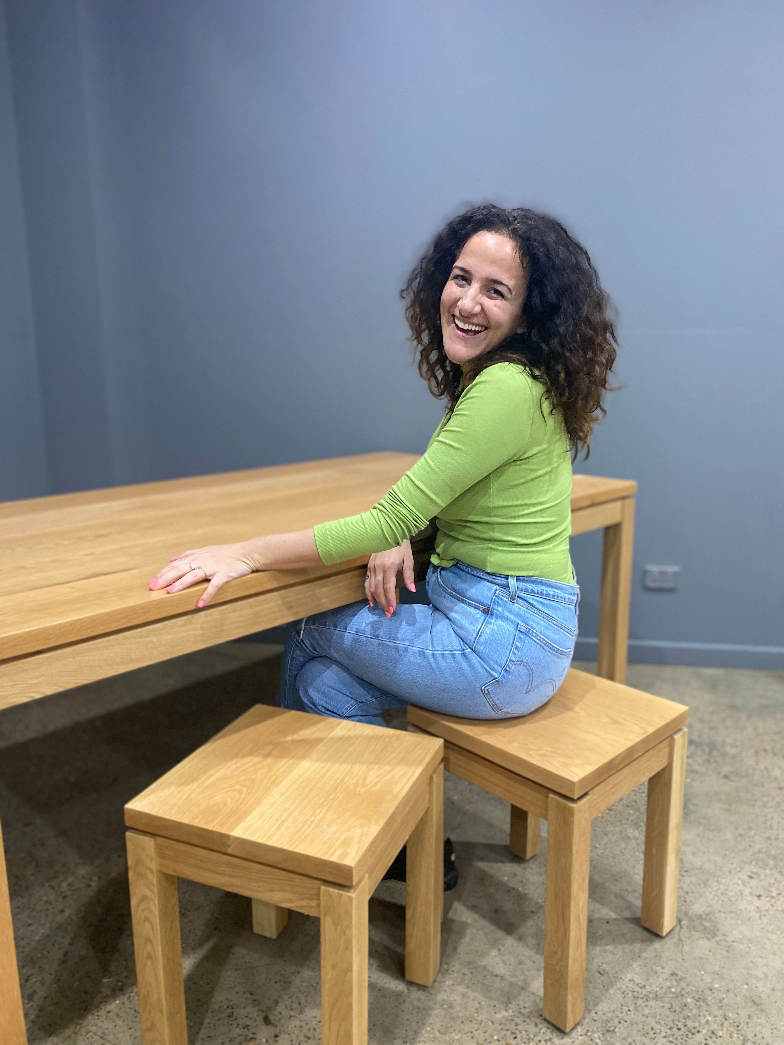 Professional home organiser sitting at custom designed dining table, wearing a green top and jeans.