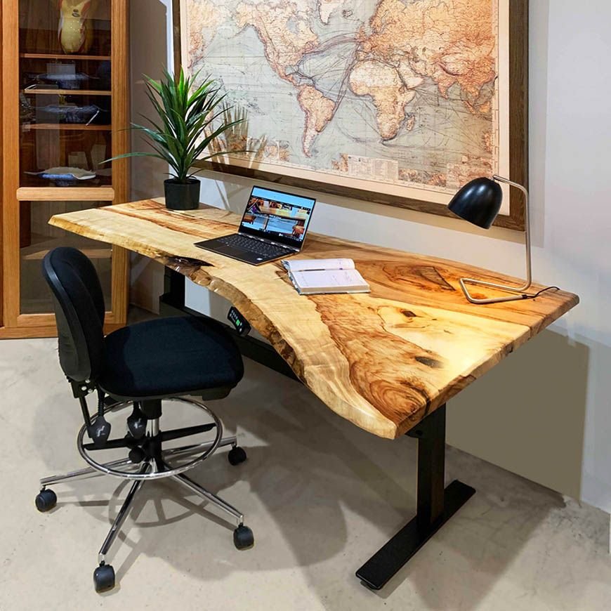 Professionally organised home office setup with a wooden live edge height adjustable desk, laptop, plant, desk lamp, chair, and world map on the wall.