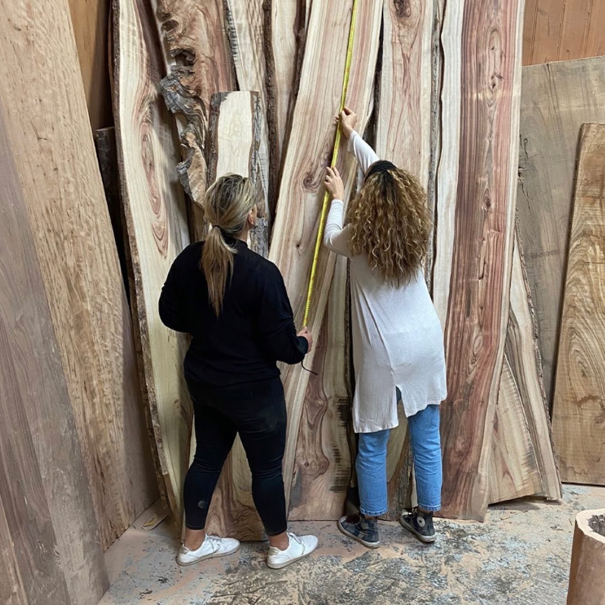 Professional organiser measuring large wooden slabs with a tape measure in a workshop.