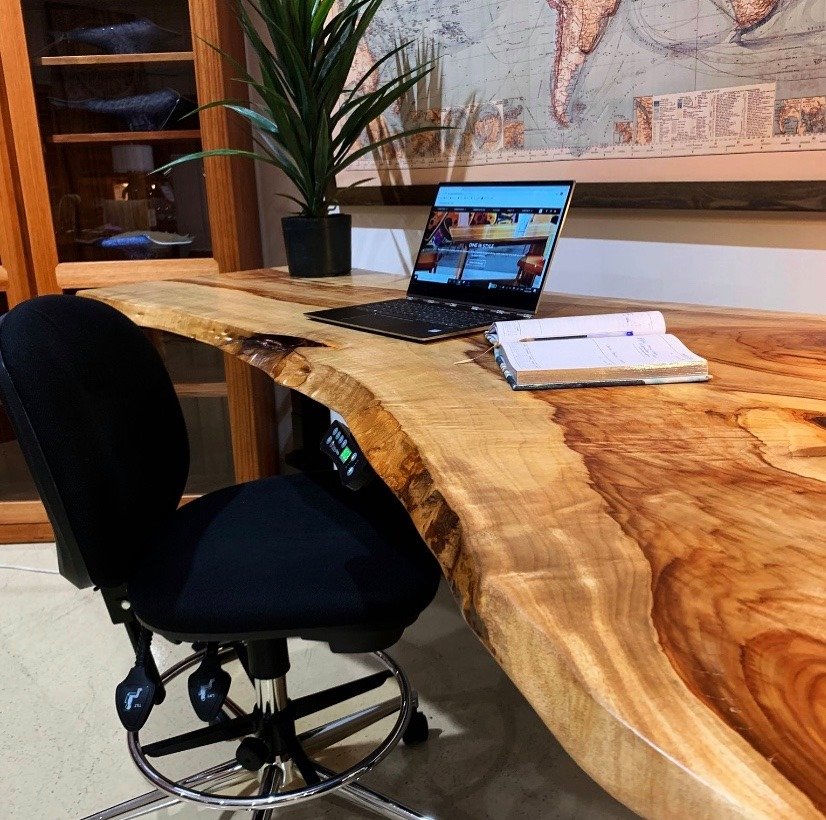 Professionally organised home office in Sydney, using a live edge height adjustable wooden desk with laptop and notebook, black office chair, potted plant, bookshelf, and map on wall.