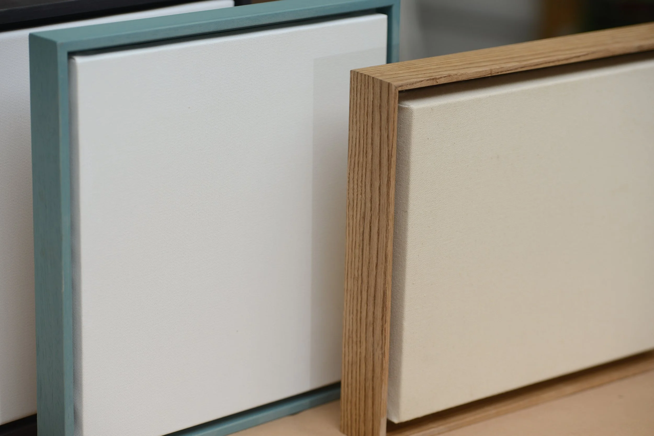 Close-up of two panels of fabric-covered acoustic tiles with wooden frames, one white and one beige, standing upright.