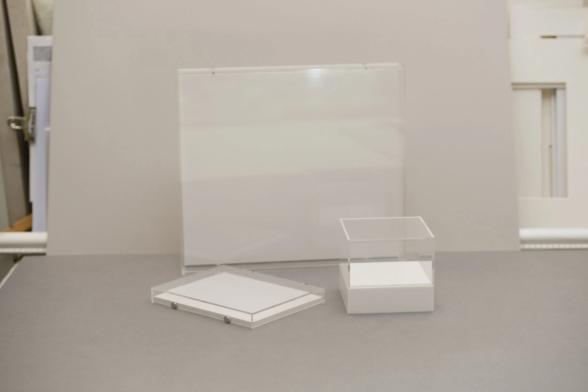 A display case with a transparent rectangle, a clear lidded box, and a large rectangular panel on a gray surface.