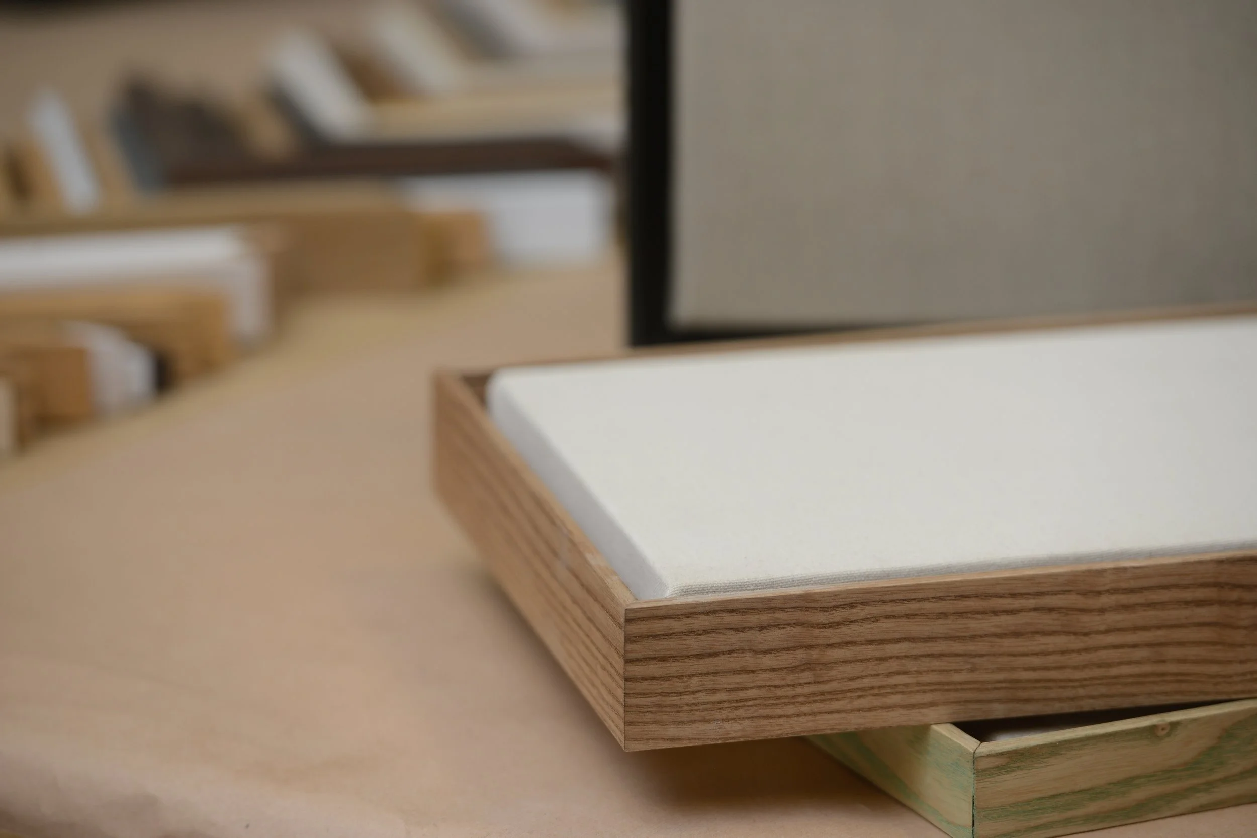Close-up of a wooden picture frame holding a white board, placed on a light-colored surface with blurred wooden shelves in the background.