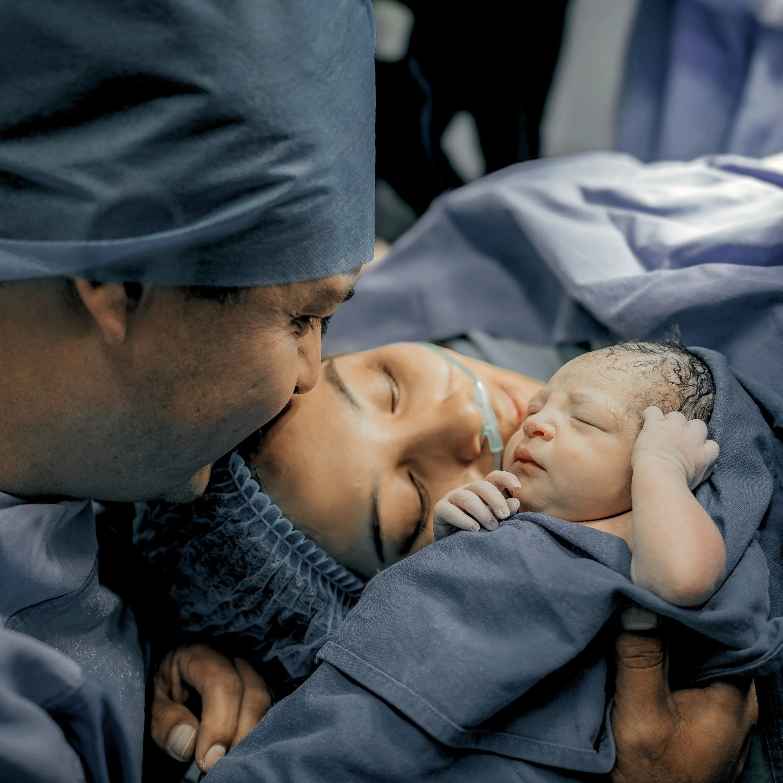 Close-up of a medical professional performing a procedure on a baby, wearing blue scrubs and a surgical cap, in a hospital setting.