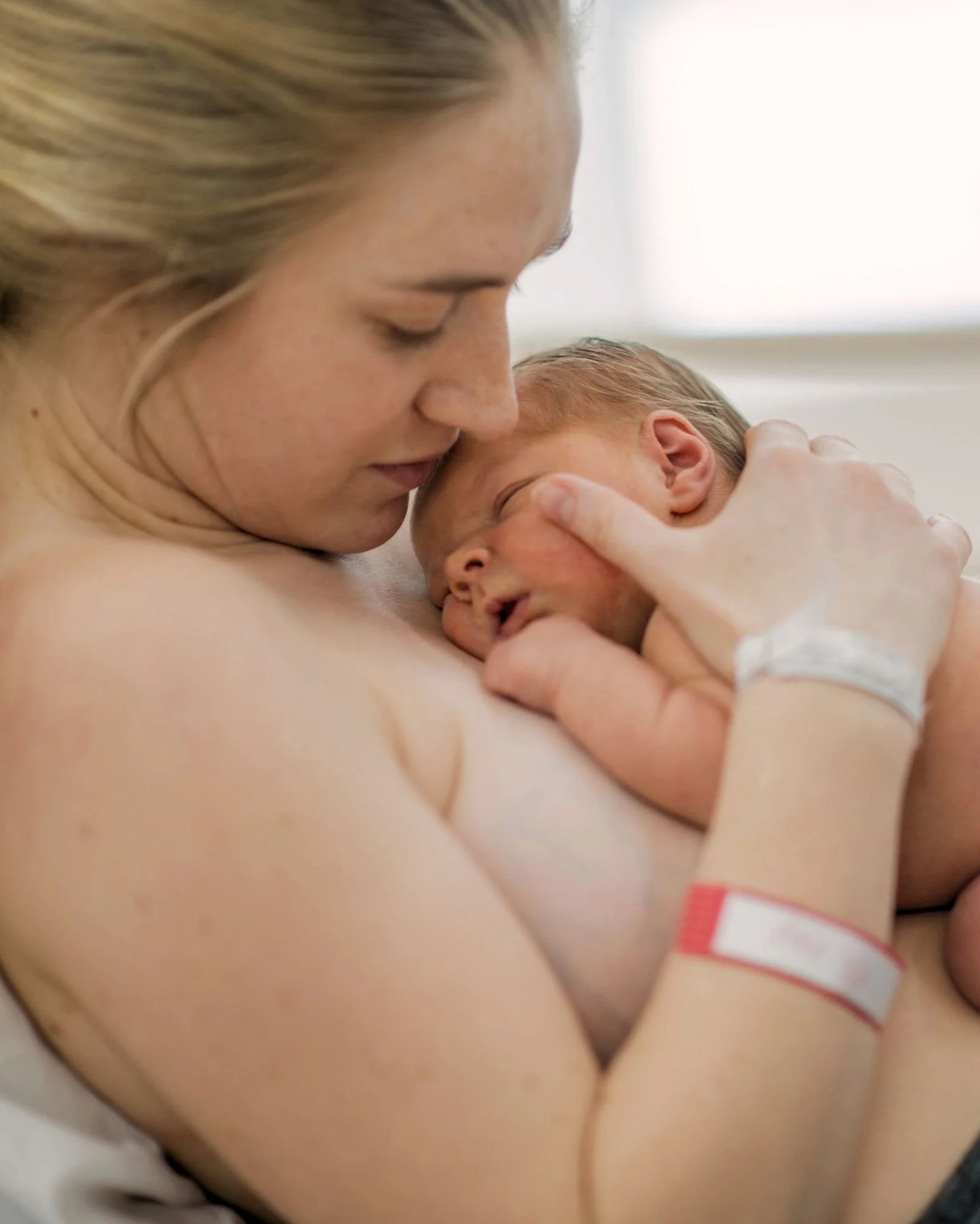 A woman holding a newborn baby with a hospital wristband on the baby's arm.