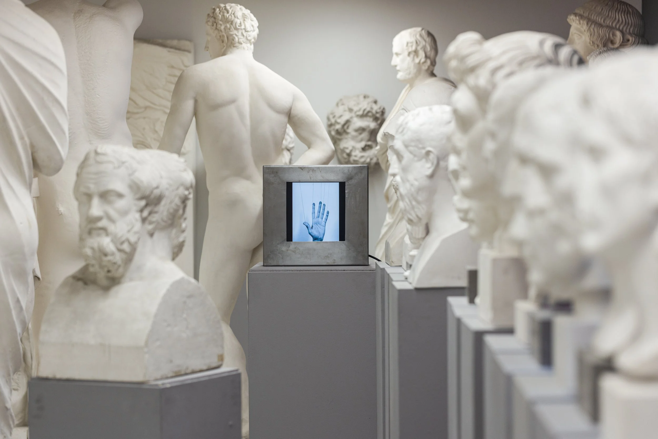 Museum mit Skulpturen und einem digitalen Bildschirm mit einer Hand im Zentrum.