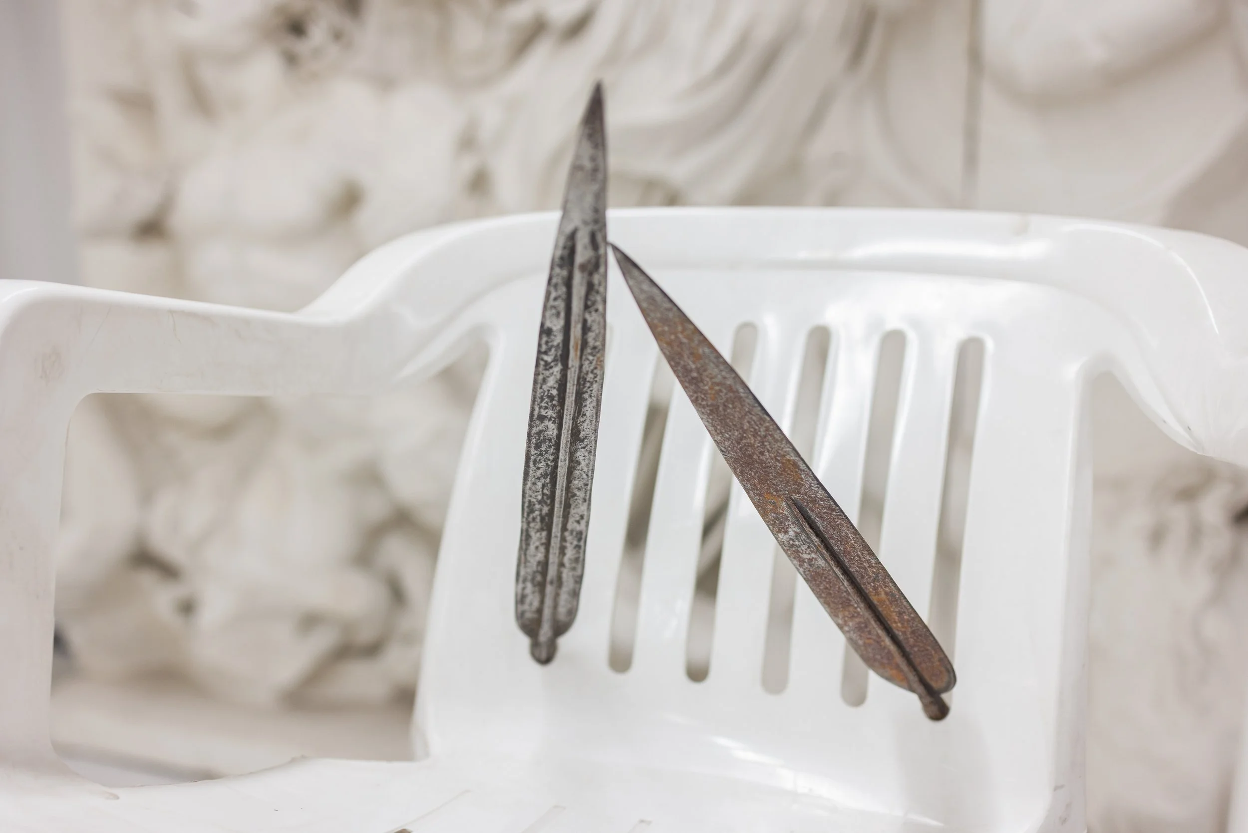 Zwei alte Messer mit rostigem Stahl liegen auf einem weißen Kunststoffstuhl.