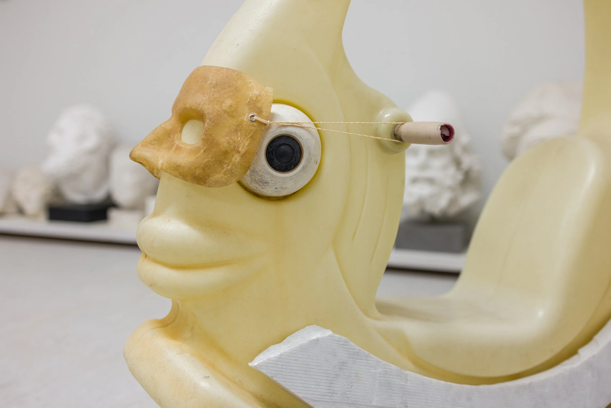 Kunststoffmodell eines menschlichen Gesichts mit einer künstlichen Augenlinse, einer Ohrmaske und Nasenart. Im Hintergrund sind weitere Skulpturen zu sehen.