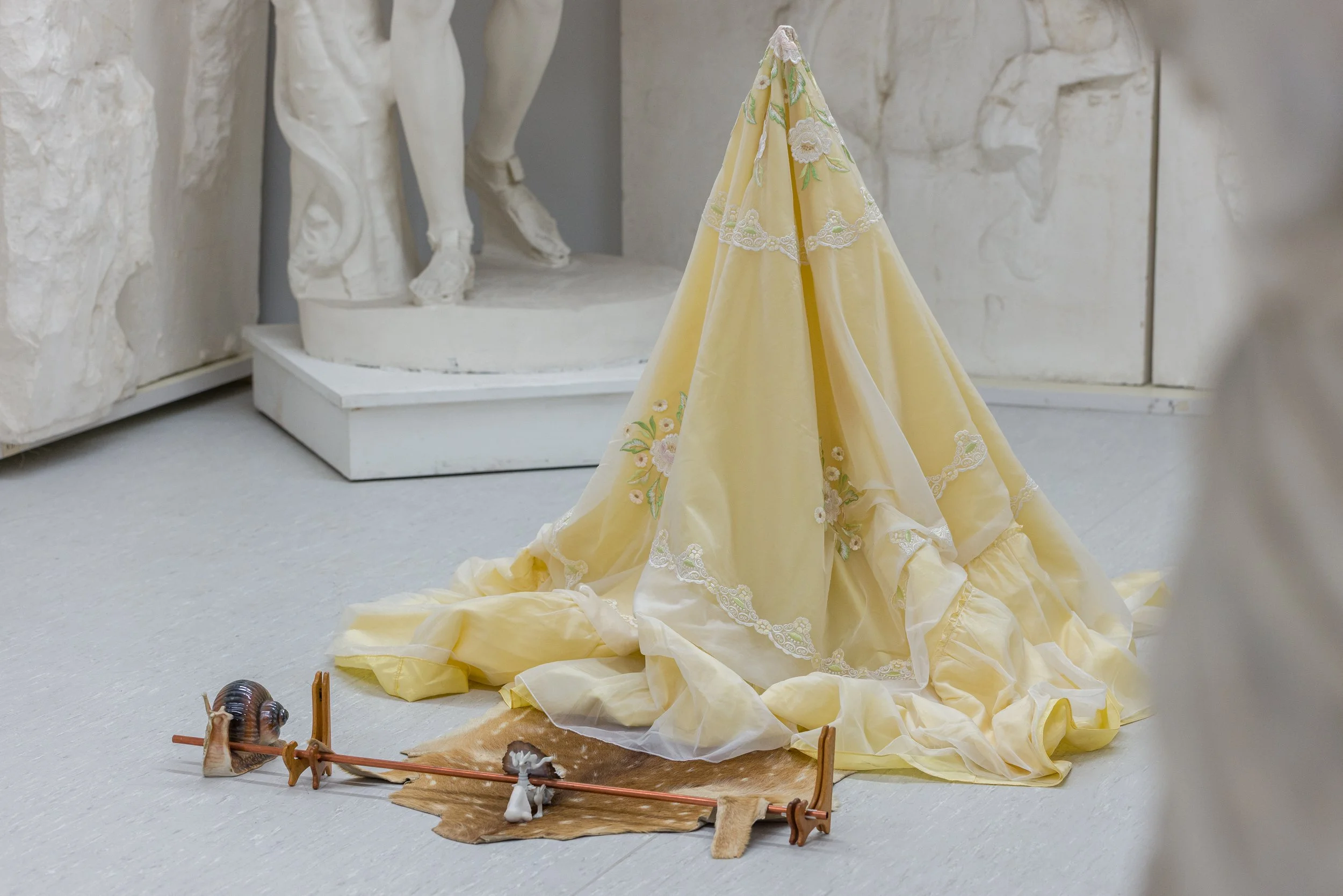 Ein gelbliches Kleid mit weißen Stickereien, auf dem Boden in einem Museum, im Vordergrund eine kleine Künstlerin im Sch******, Beobachtung eines ausgestellten Outfits.