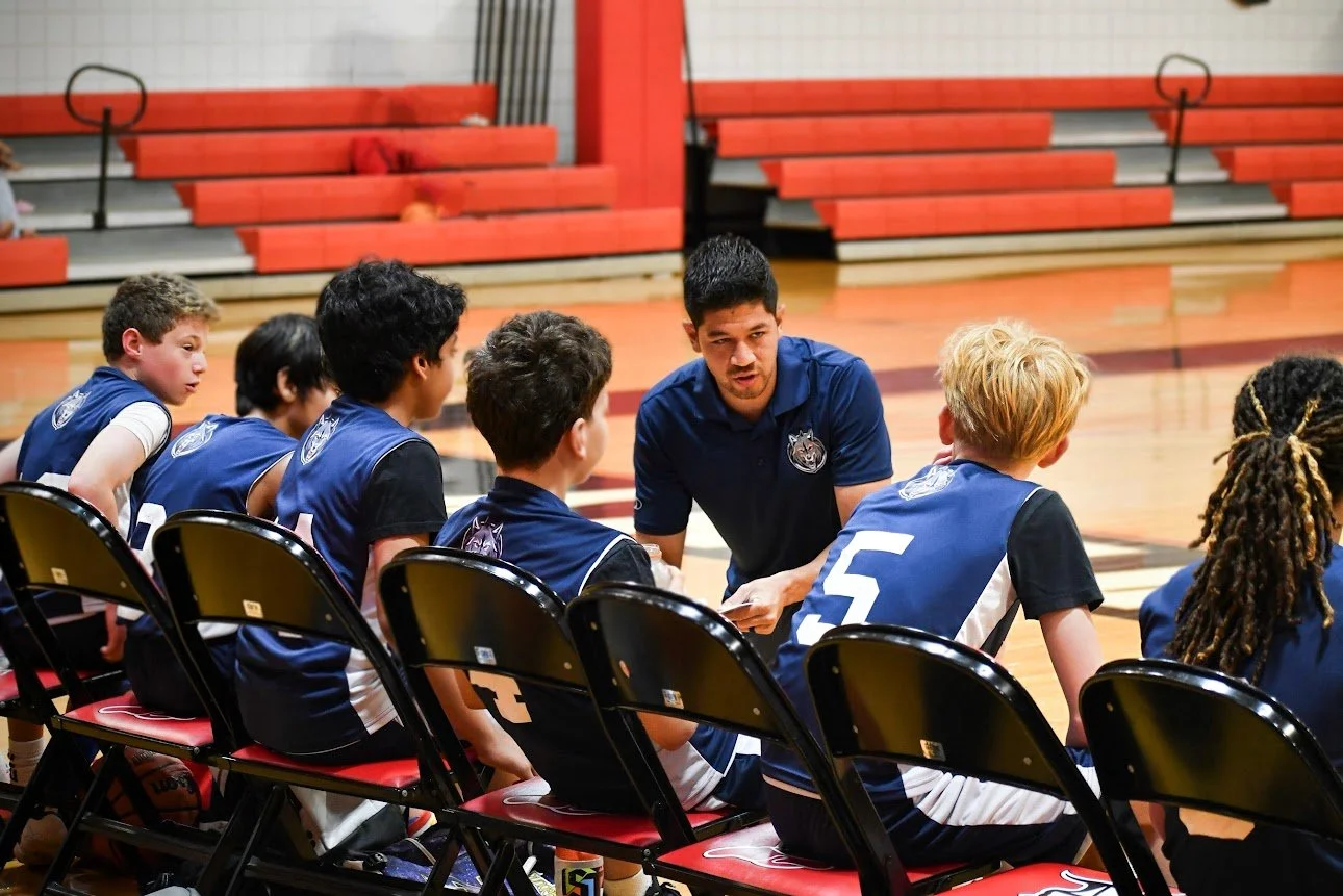 A coach talking to young basketball players during a game or practice in a gymnasium.