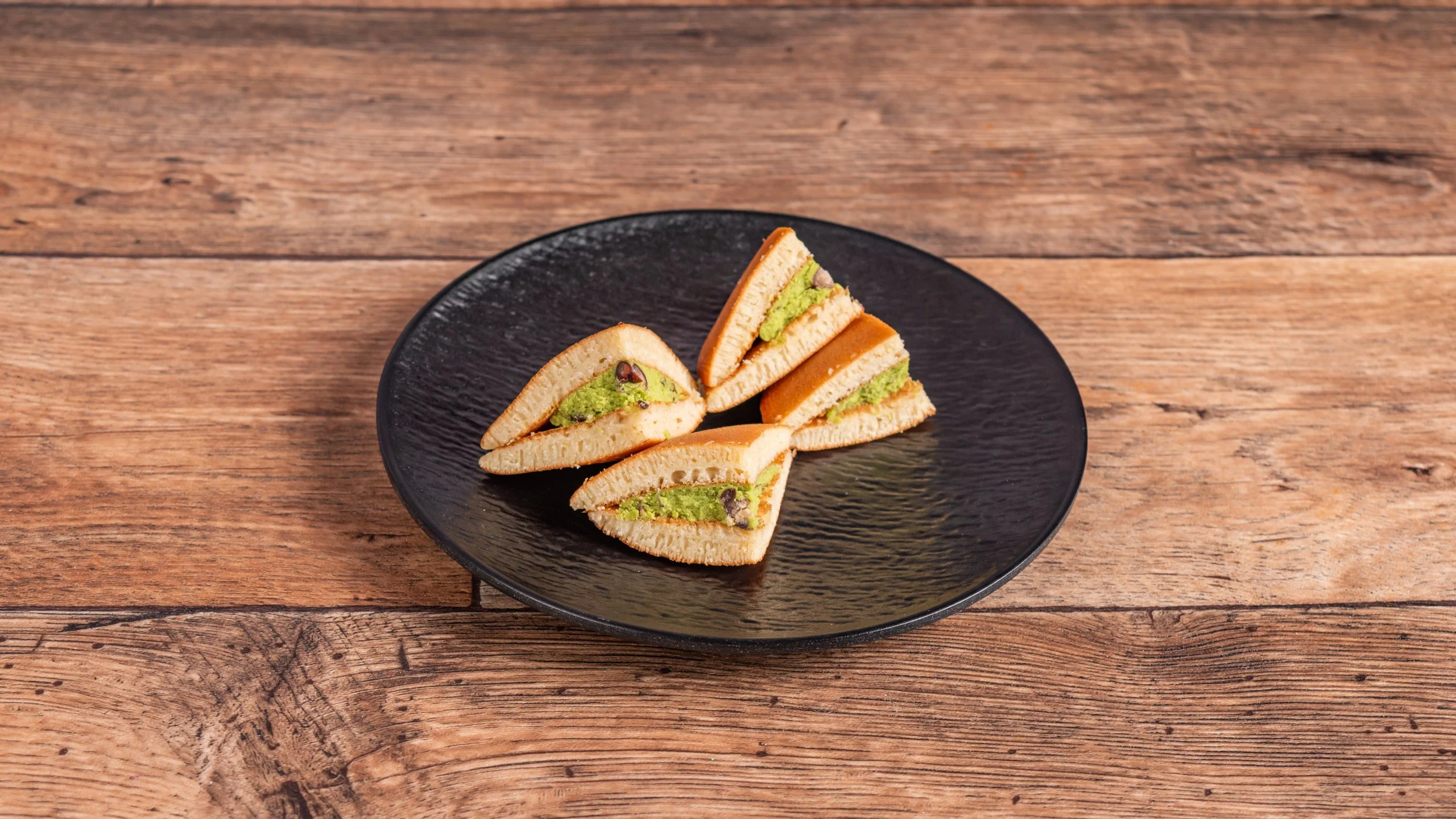 Four slices of green tea and red bean sandwich cookies on a black plate placed on a wooden table.