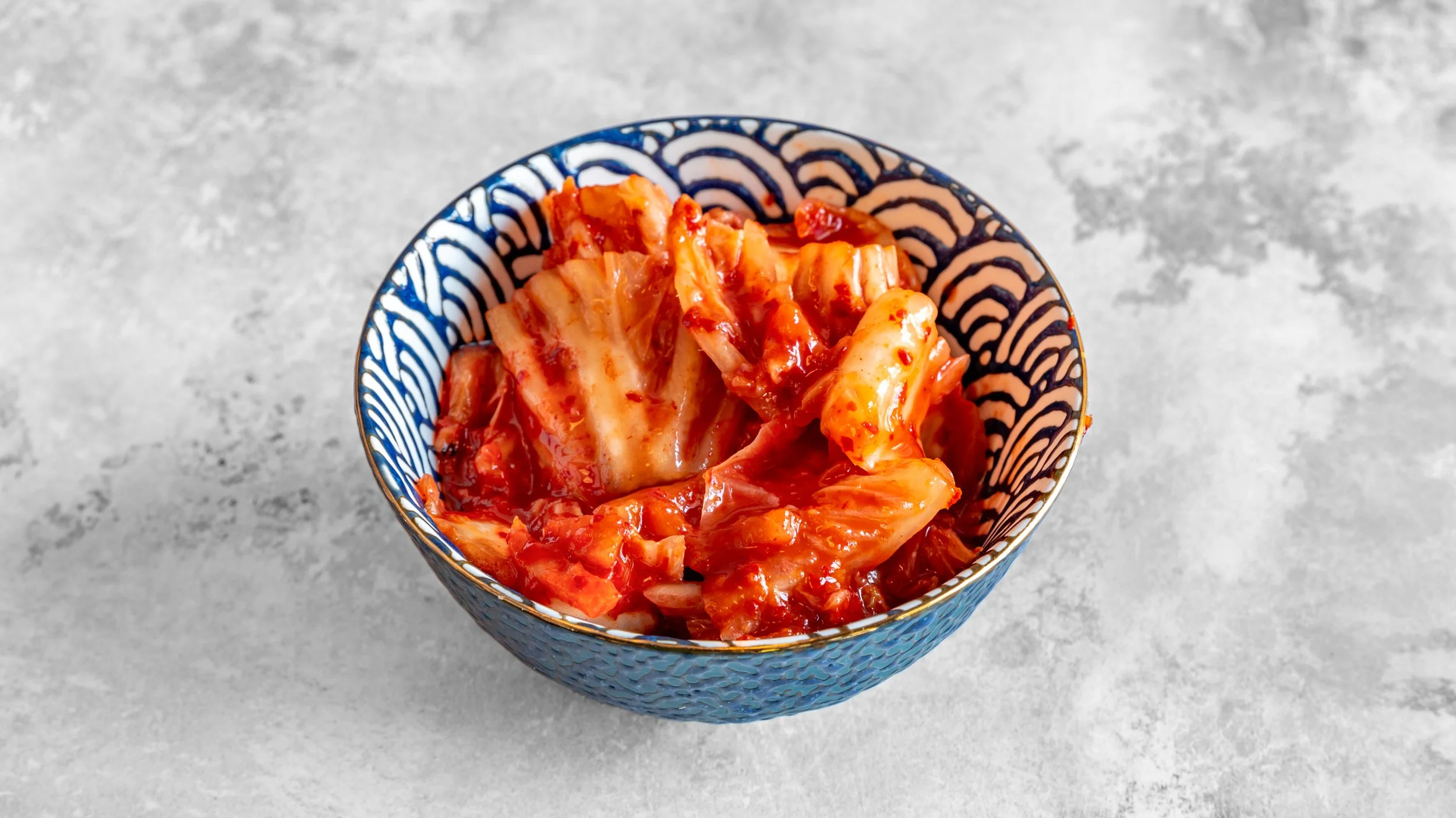A bowl of kimchi on a gray surface.