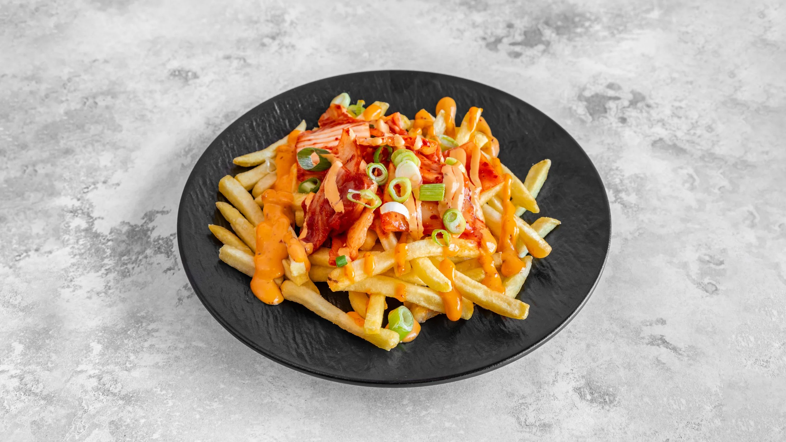 Plate of French fries topped with sliced green onions,kimchi, spicy sauce.