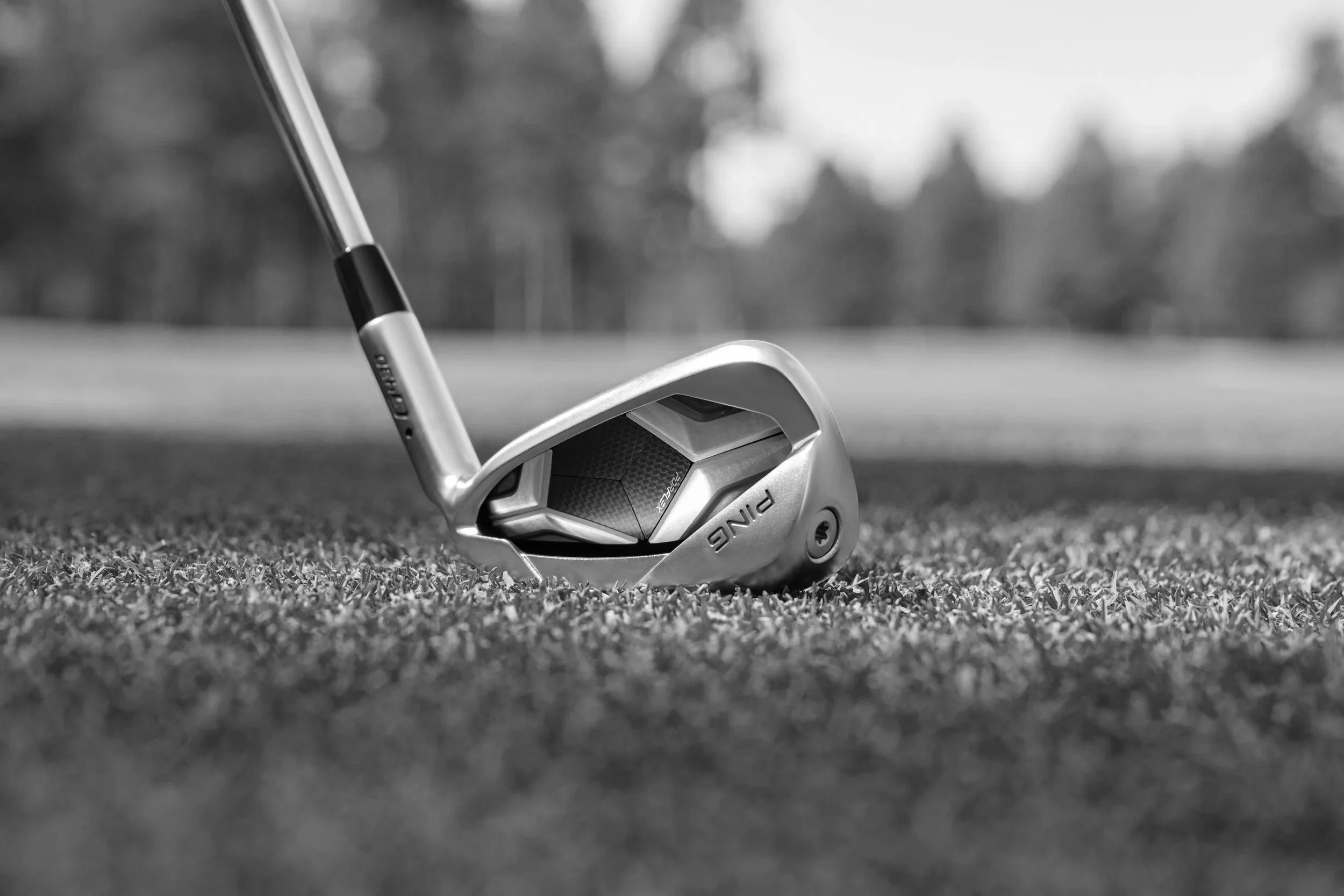 Golf club with a golf ball in a golf course setting on green grass, with trees in the background.