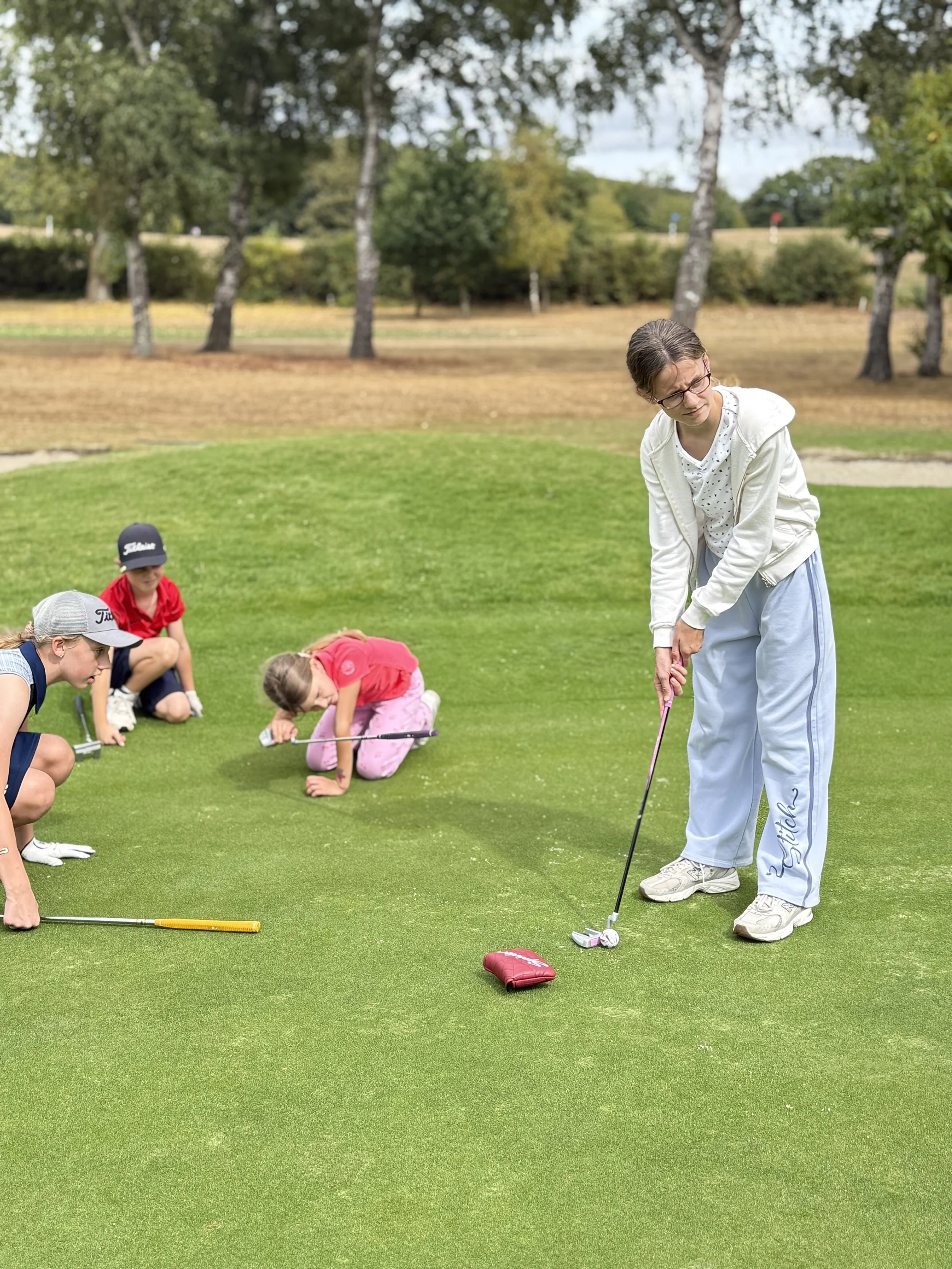 Young boy practicing putting on a golf green under cloudy sky.