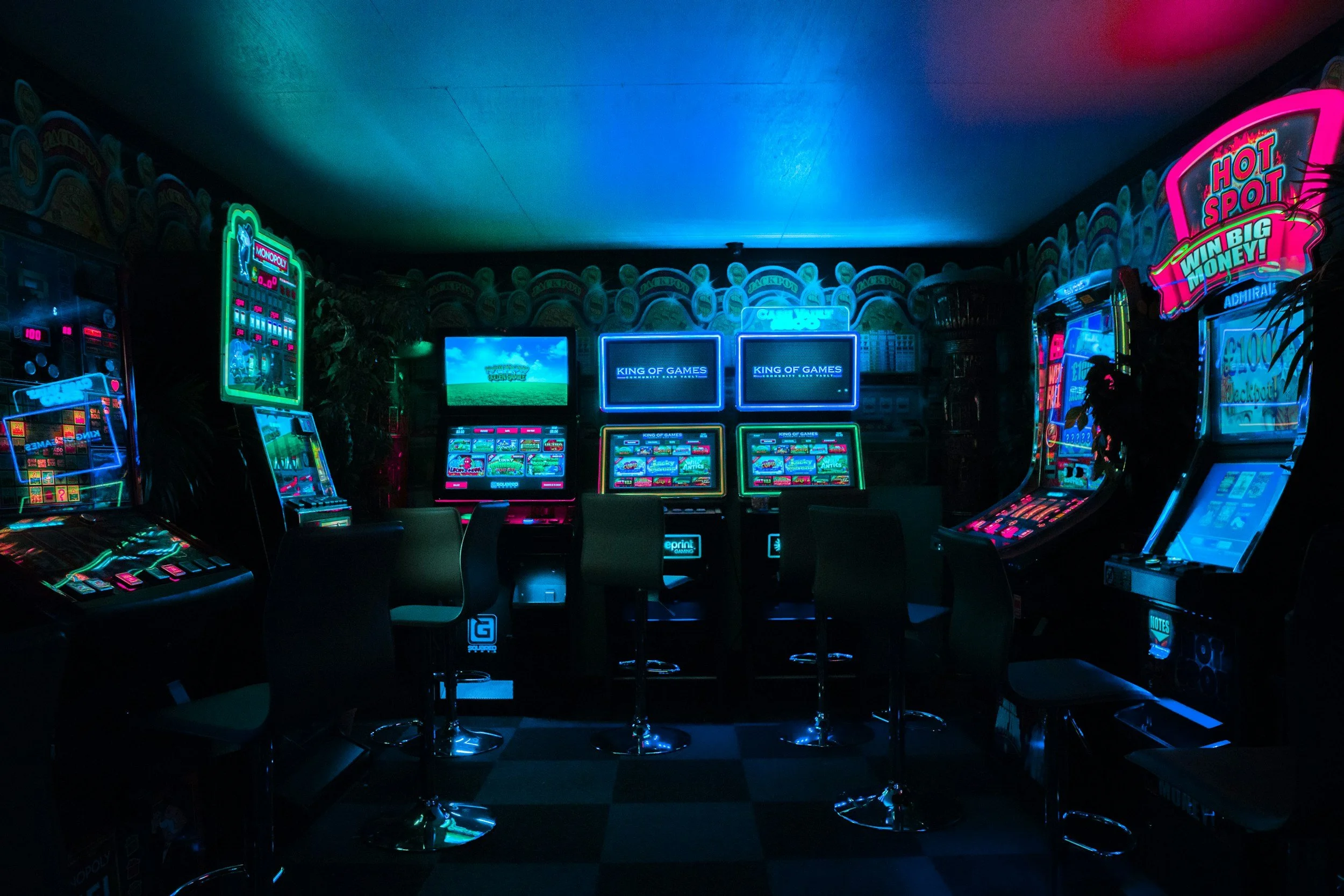 A dimly lit arcade room with multiple neon-lit gaming machines and chairs.