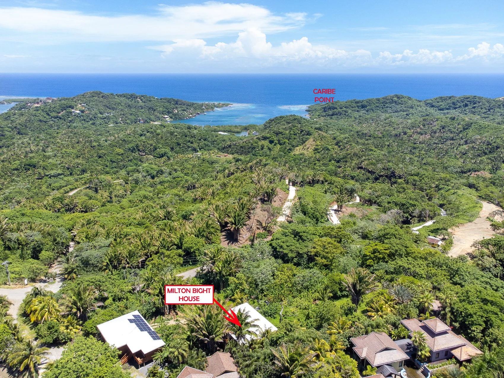 Aerial view of a lush green tropical landscape with labeled points: Milton Bight House in the foreground with solar panels on the roof, Caribbe Point in the distance near the coastline, and the ocean in the background.
