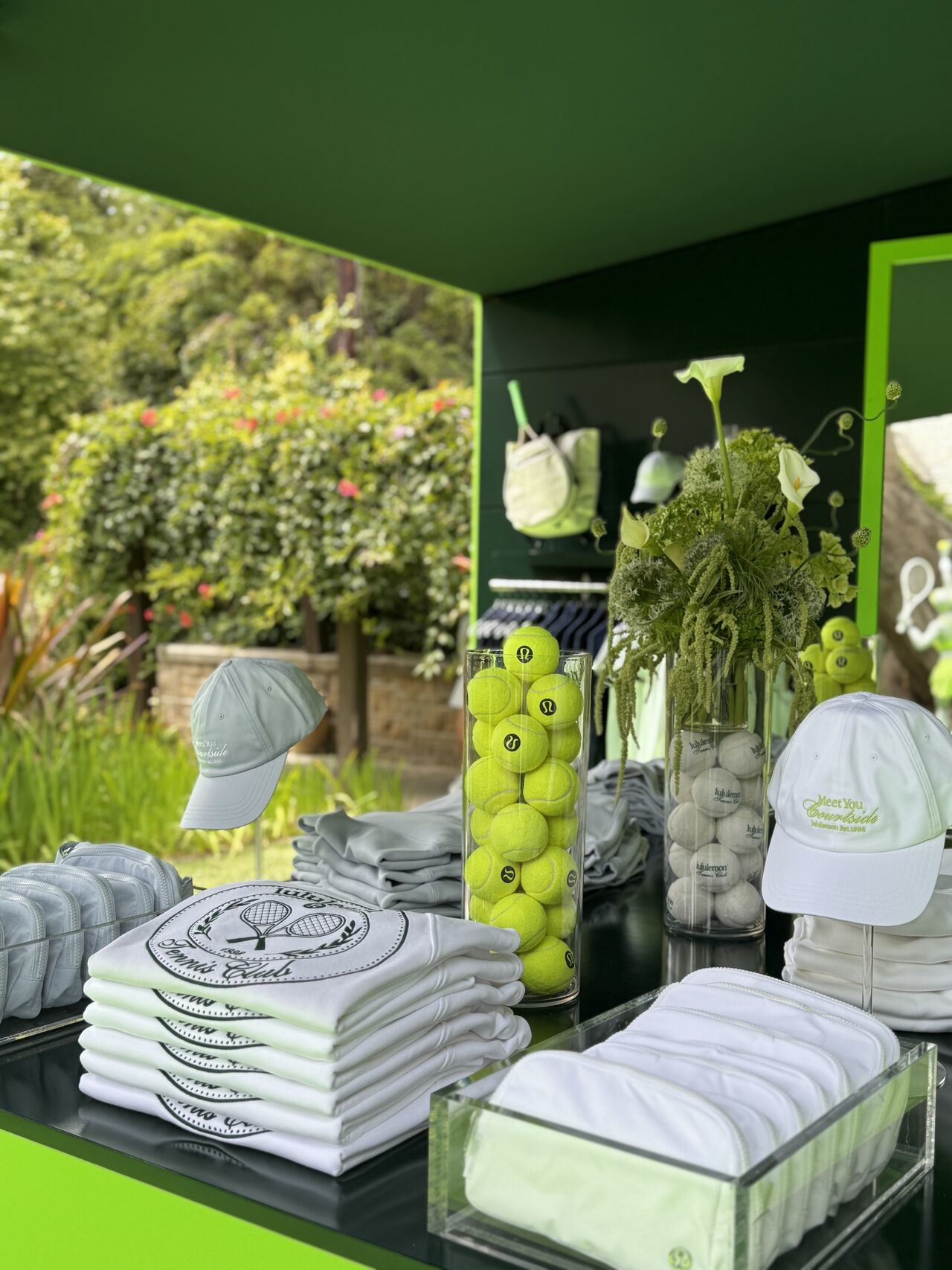 Lululemon outdoor table displaying crewnecks with embroidery, tennis balls, bags, and hats with the New Gen Prep feel.