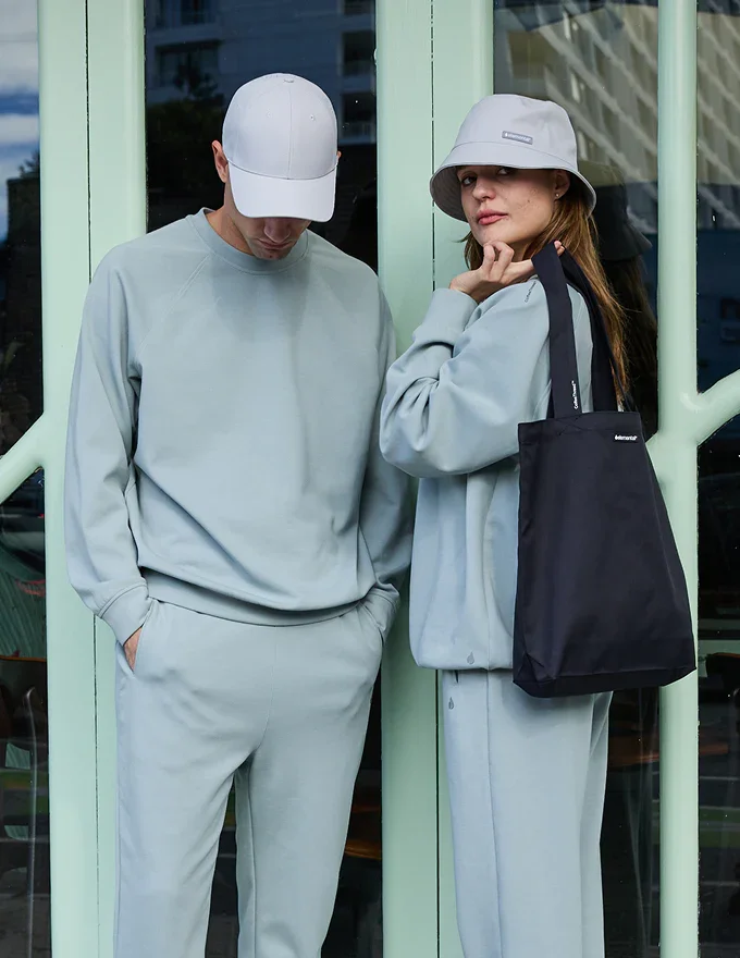 Two models in light blue sweat sets, and hats, one holding a navy blue tote bag, all created by CoffeeThread™ by Elemental, showcasing sustainable and trend-forward fashion.