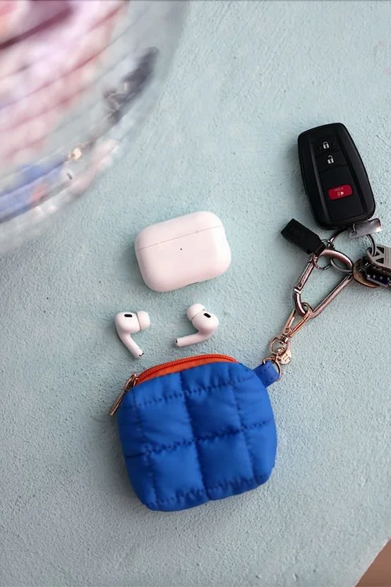 Mini puffer pouch designed for AirPods with clip attachment, shown clipped to keys, demonstrating modular accessory that adds storage to existing items.