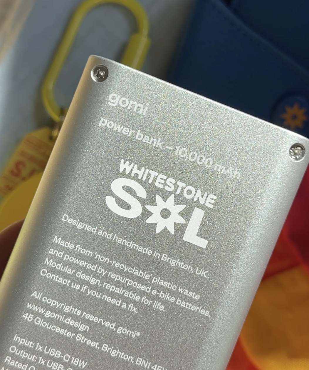A close-up shot of the matte silver aluminum backing of a Gomi power bank. The text "gomi power bank – 10,000 mAh" and the "WHITESTONE SOL" logo are precision laser-engraved onto the surface along with sustainability details.